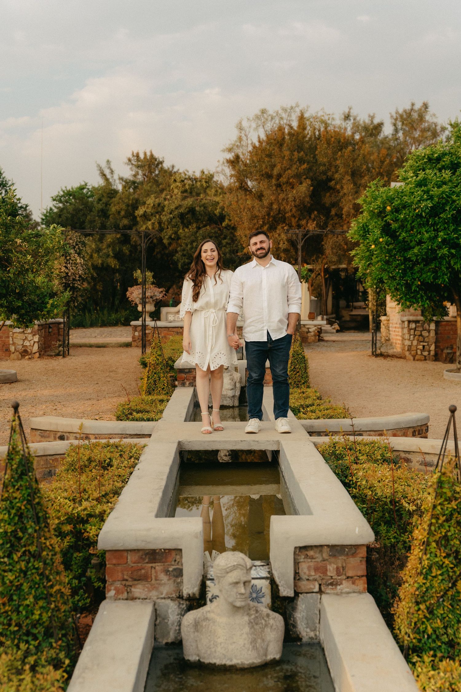 A couple poses together in a rustic garden with concrete structures and greenery.