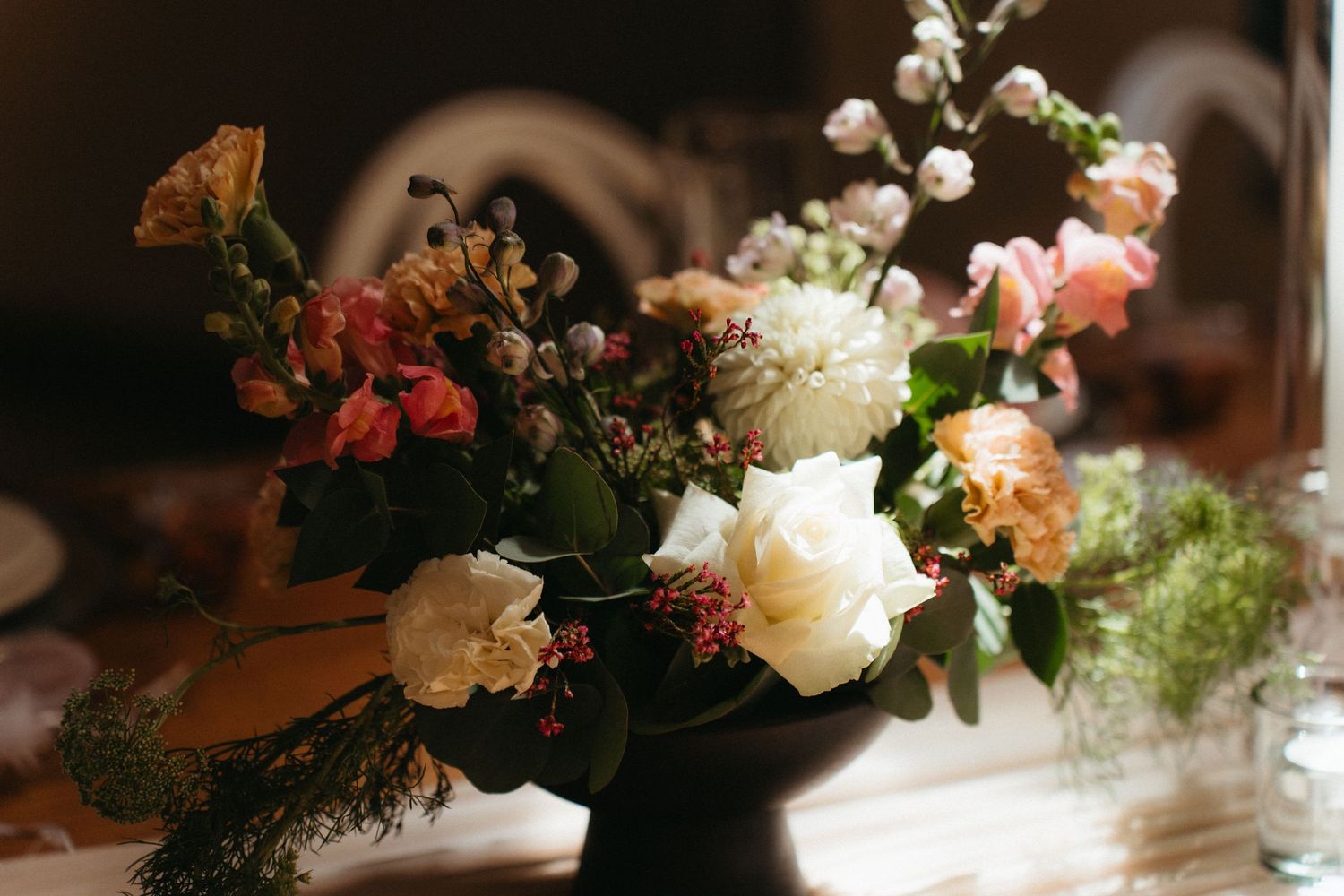 A series of elegant floral arrangements with soft roses and greenery line up along a sunlit surface creating a romantic ambiance.