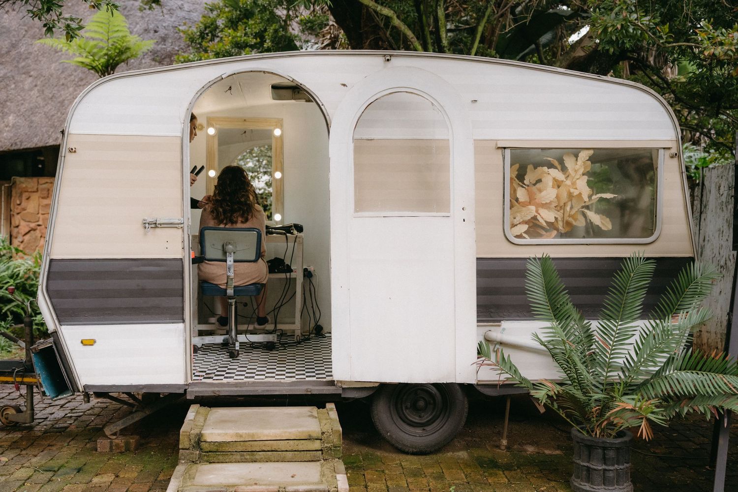 Vintage white caravan trailer set up in a garden with plants and decorative elements.