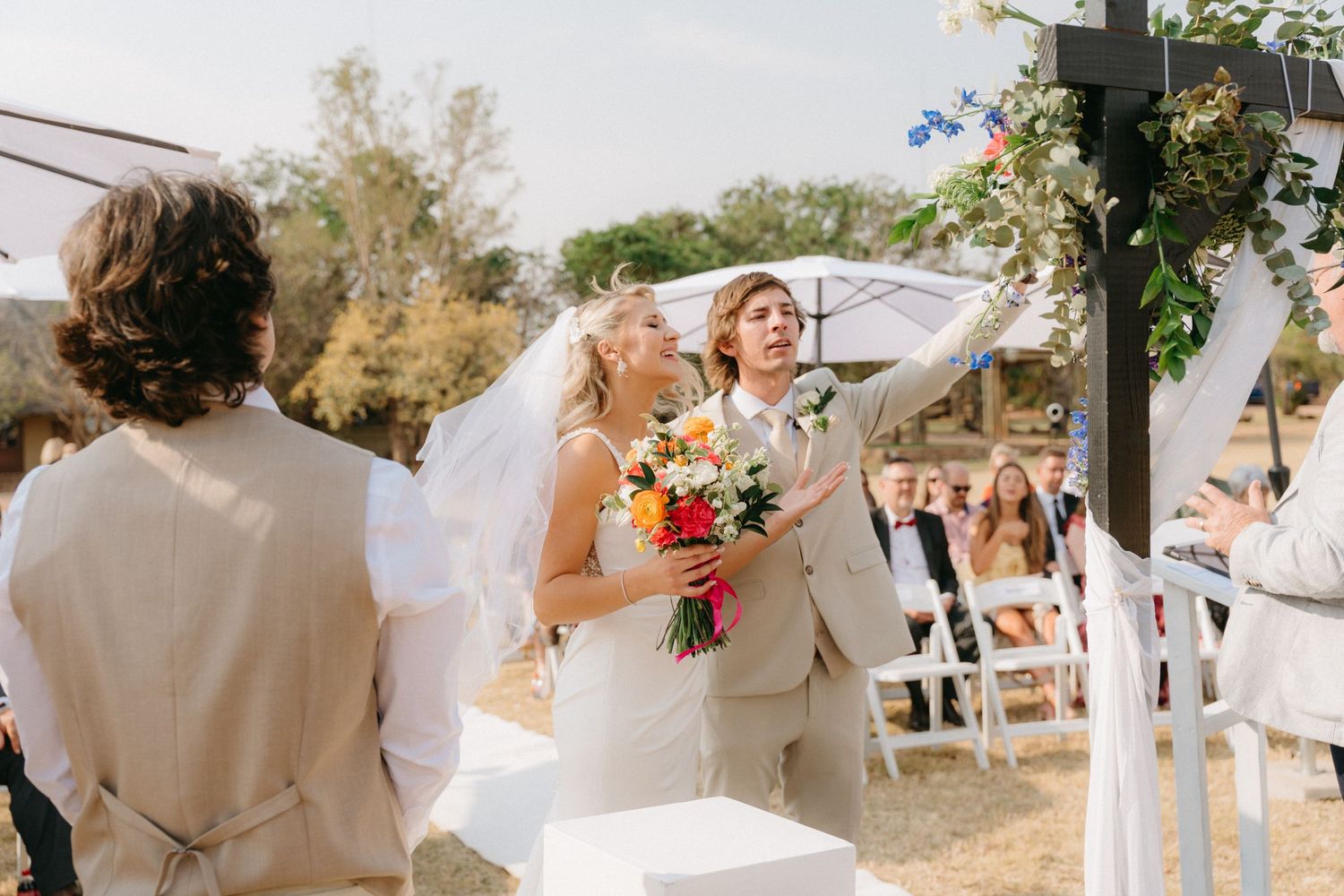 Outdoor wedding ceremony setup with white chairs and floral arrangements under a clear blue sky.