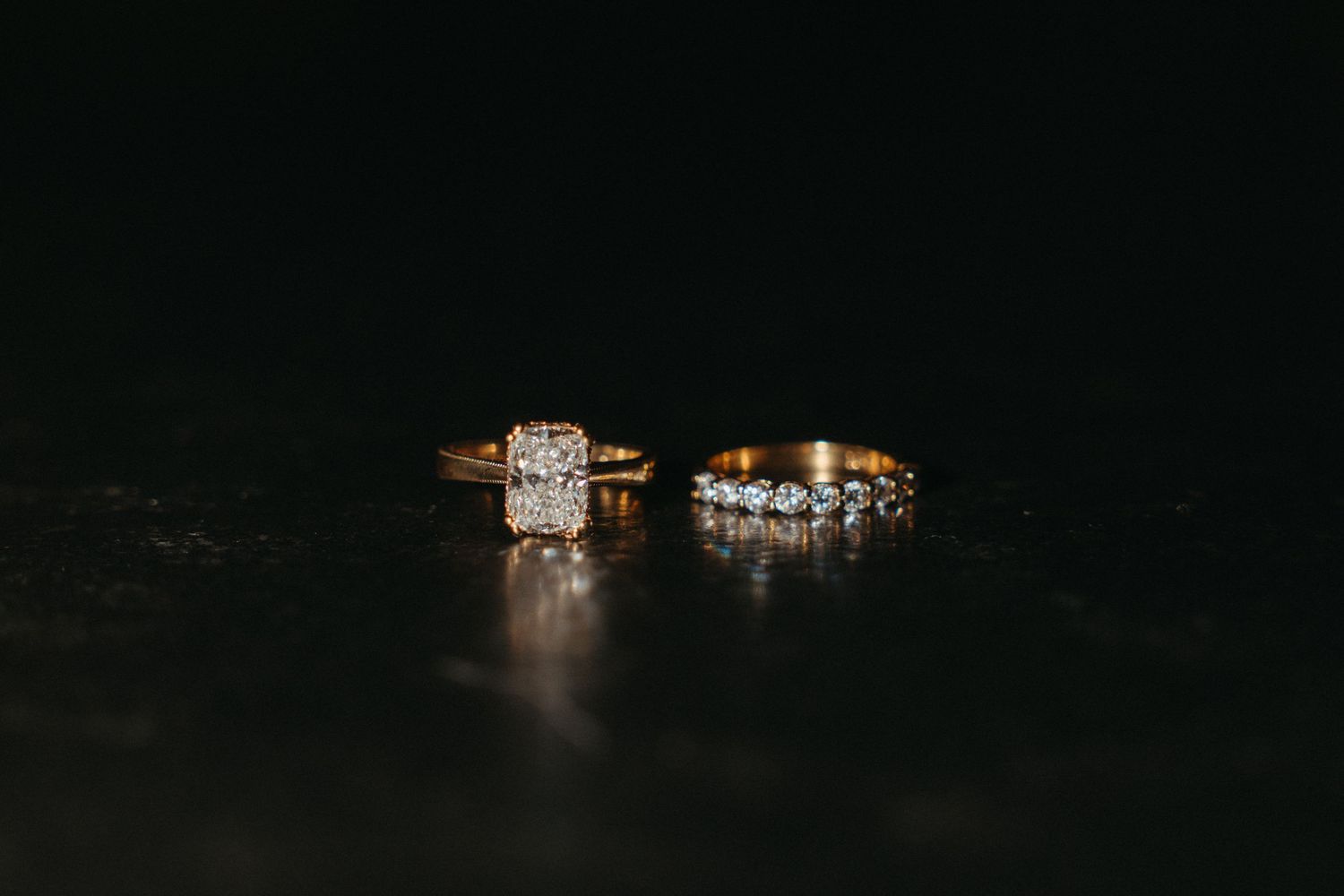Two gold diamond wedding rings displayed on dark reflective surface in dramatic lighting at Beechwood Gardens in Johannesburg.