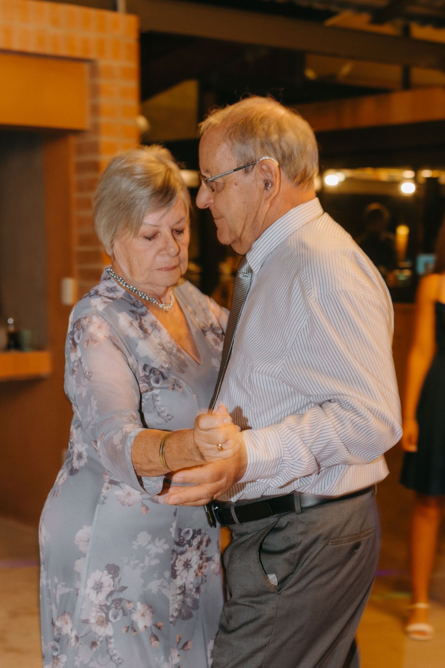 An elderly couple shares an intimate slow dance together at an indoor venue.