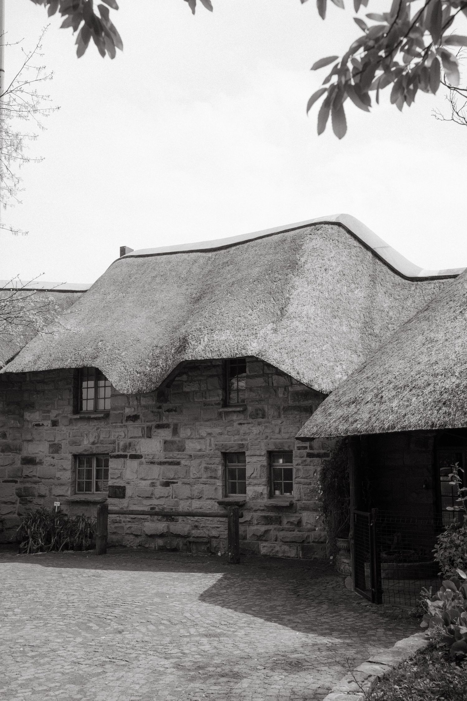 Historic stone buildings with thatched roofs shown in a series of black and white architectural photographs.