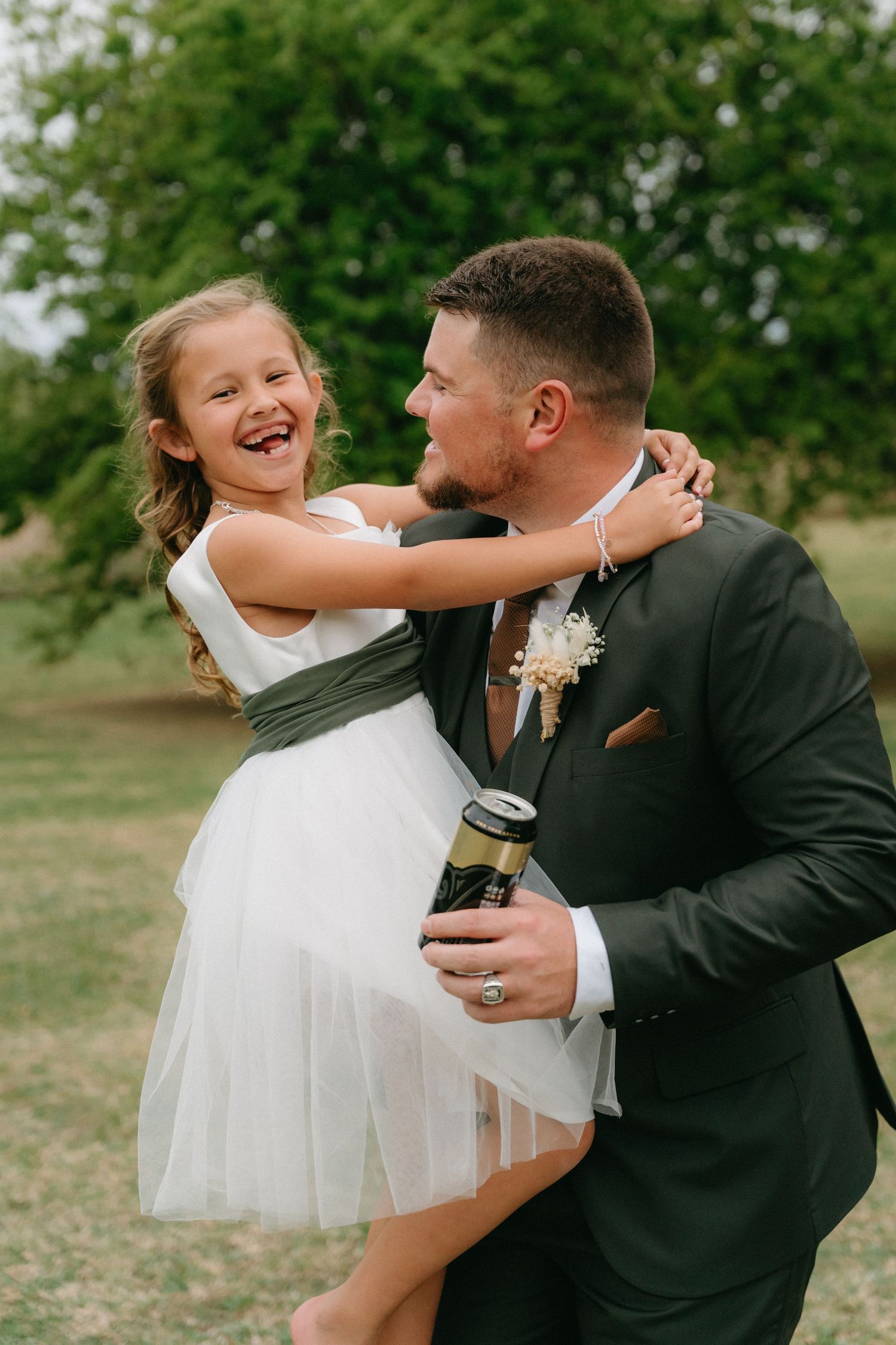 Sweet candid moment between a father and flower girl at outdoor wedding.