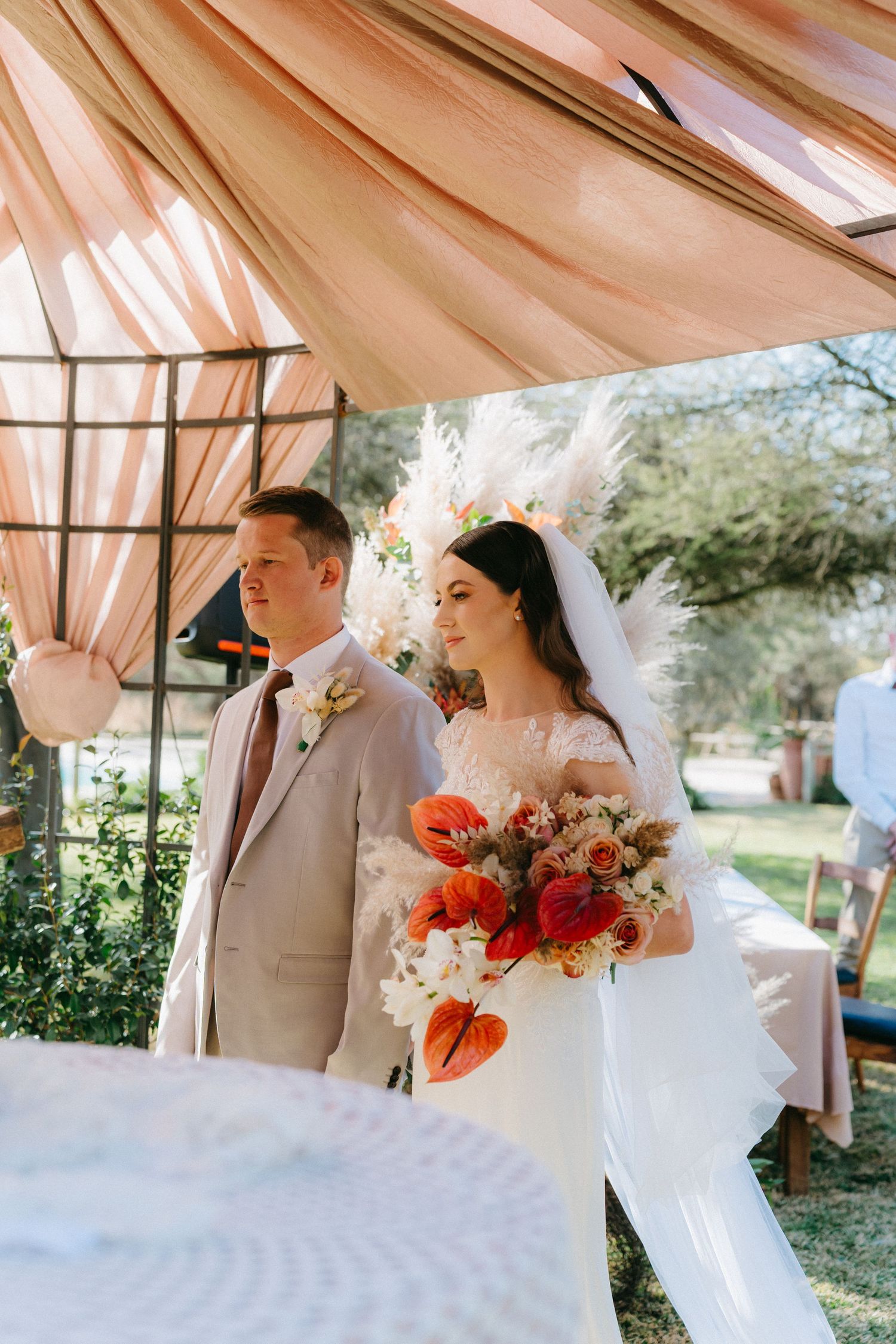A wedding ceremony under a draped tent with coral fabric and natural lighting.