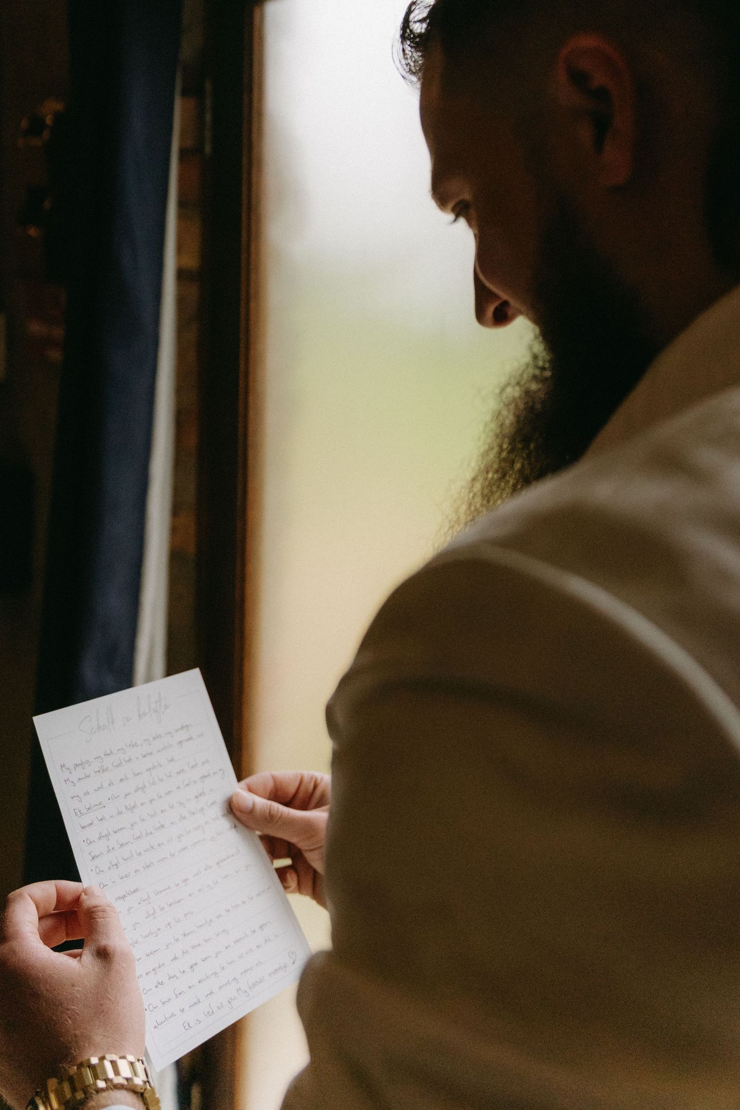 Someone holding and reading handwritten notes while standing near a window.