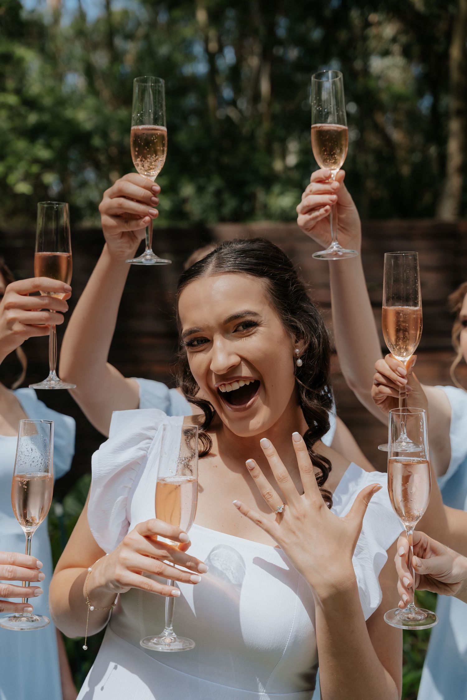 A group in white attire raises champagne glasses in a celebratory toast outdoors.