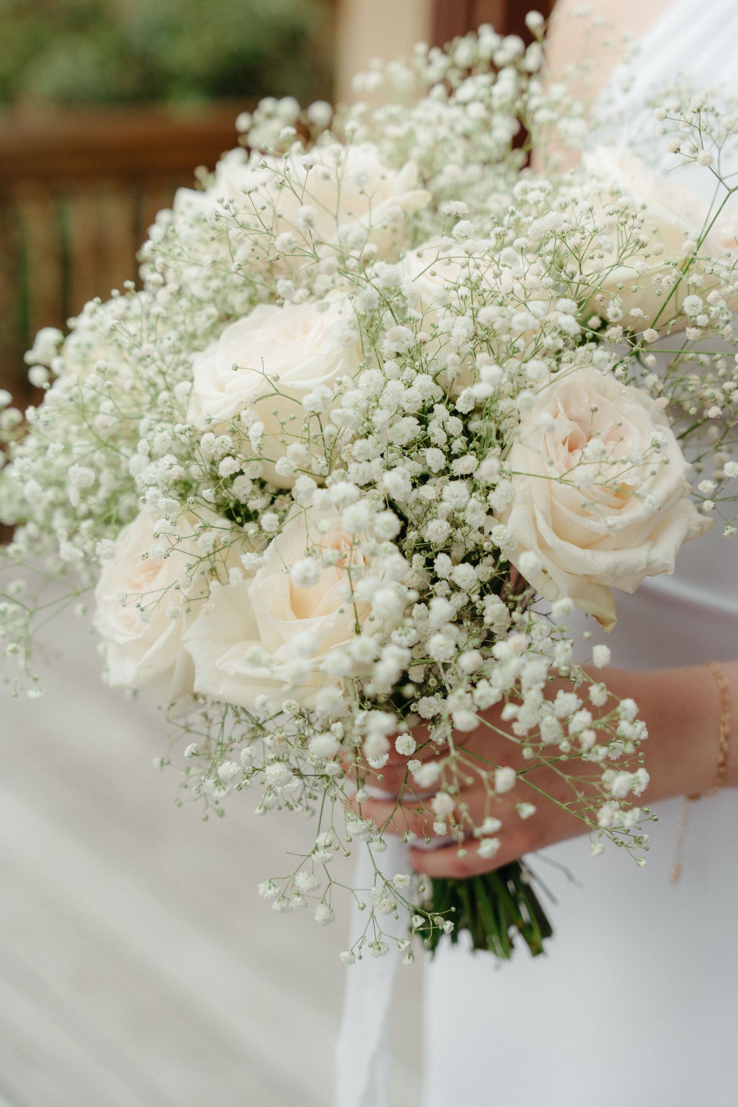 Elegant white rose and baby's breath wedding bouquet held against soft fabric.