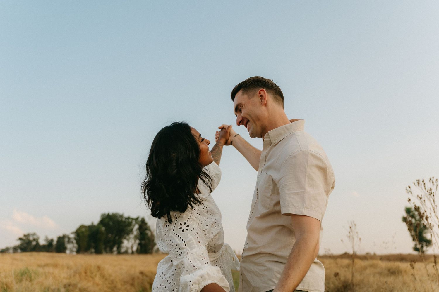 Happy couple embracing and smiling in a summer field against blue sky.