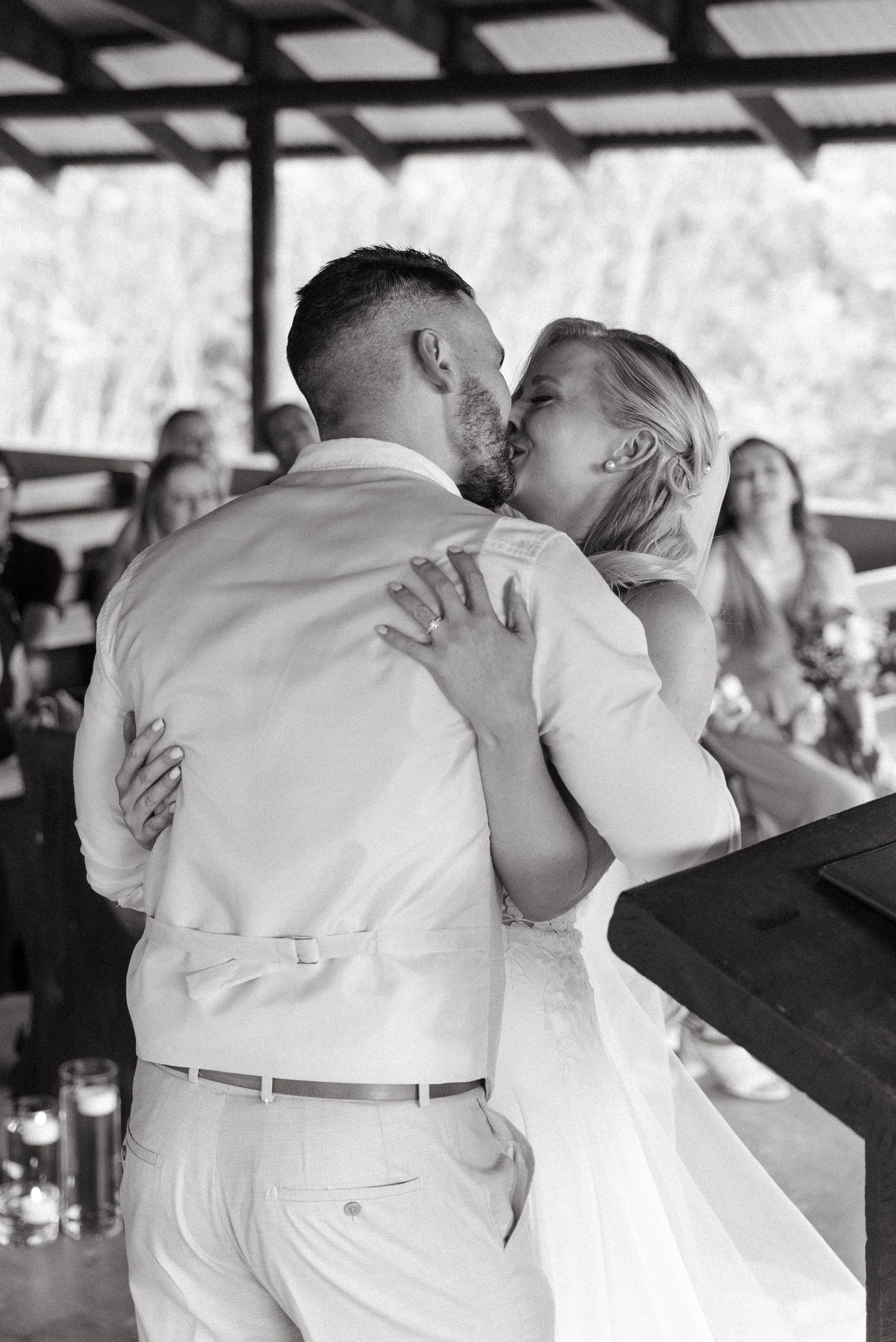 Emotional embrace shared during wedding reception with guests in background.