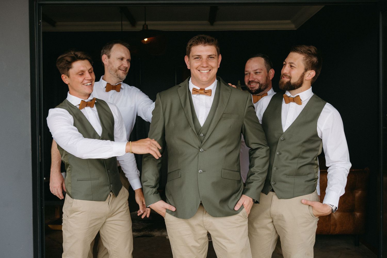 Groomsmen in matching olive vests and khakis pose together before the wedding ceremony.