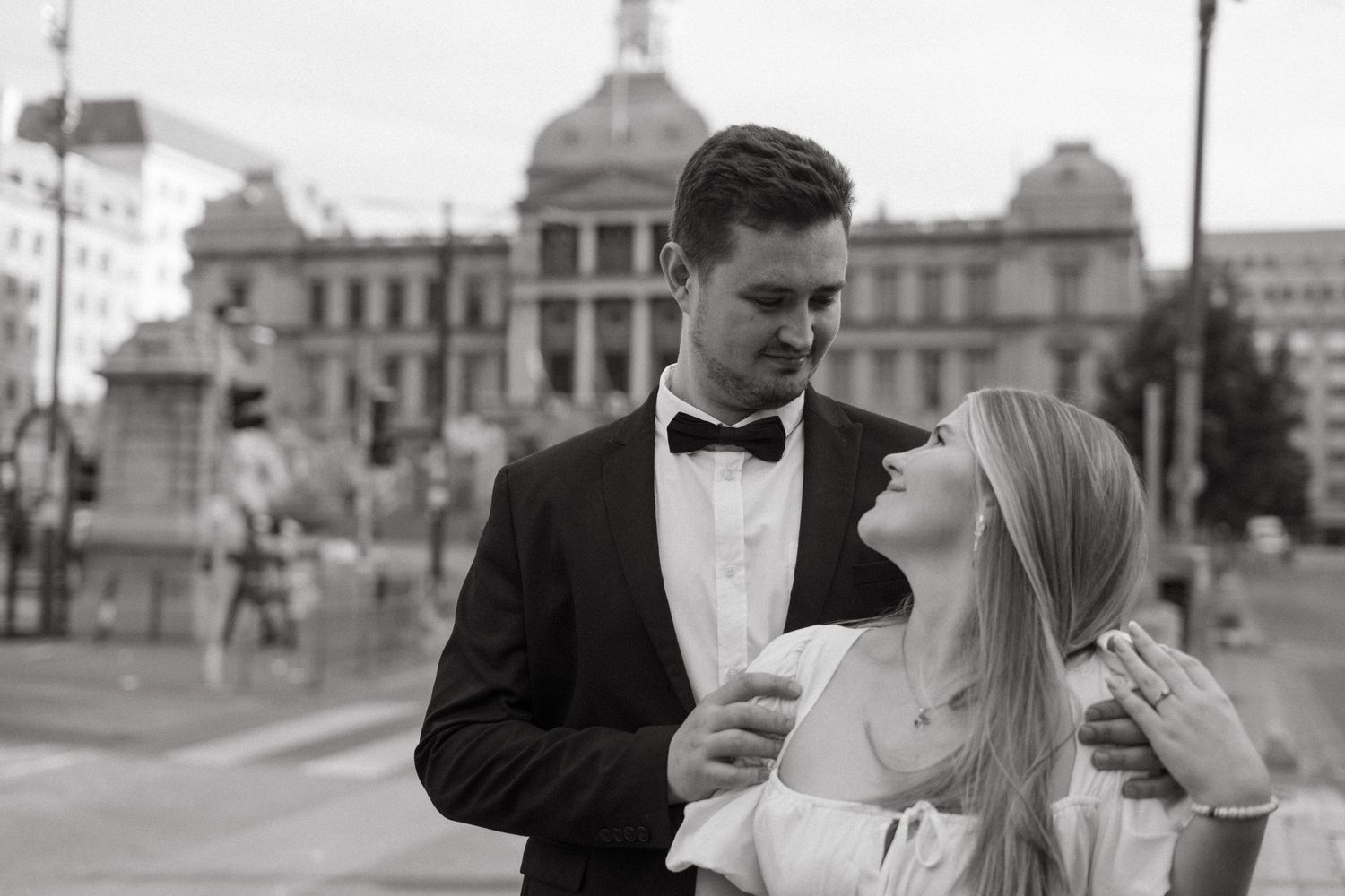 A black and white photo captures an elegant couple posing in front of a domed government building.