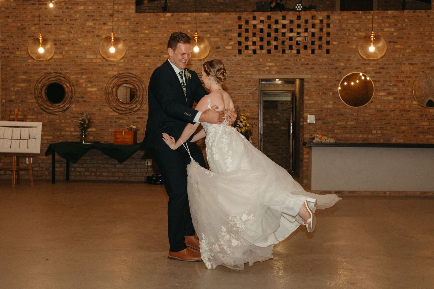 A romantic dance spin captured in warm lighting at a rustic brick reception venue.