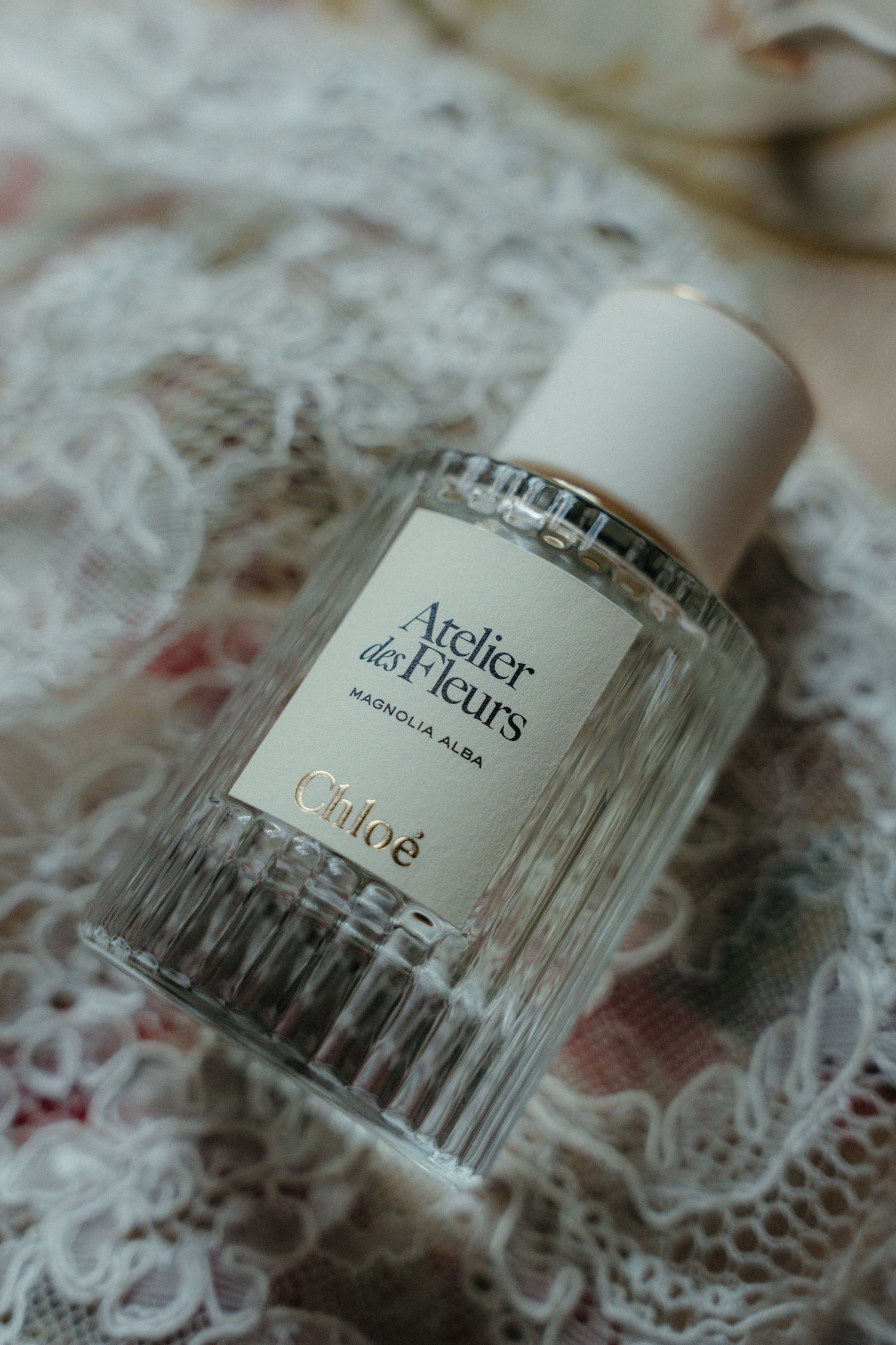Chloé Atelier des Fleurs Magnolia Alba perfume bottle on delicate lace fabric background.
