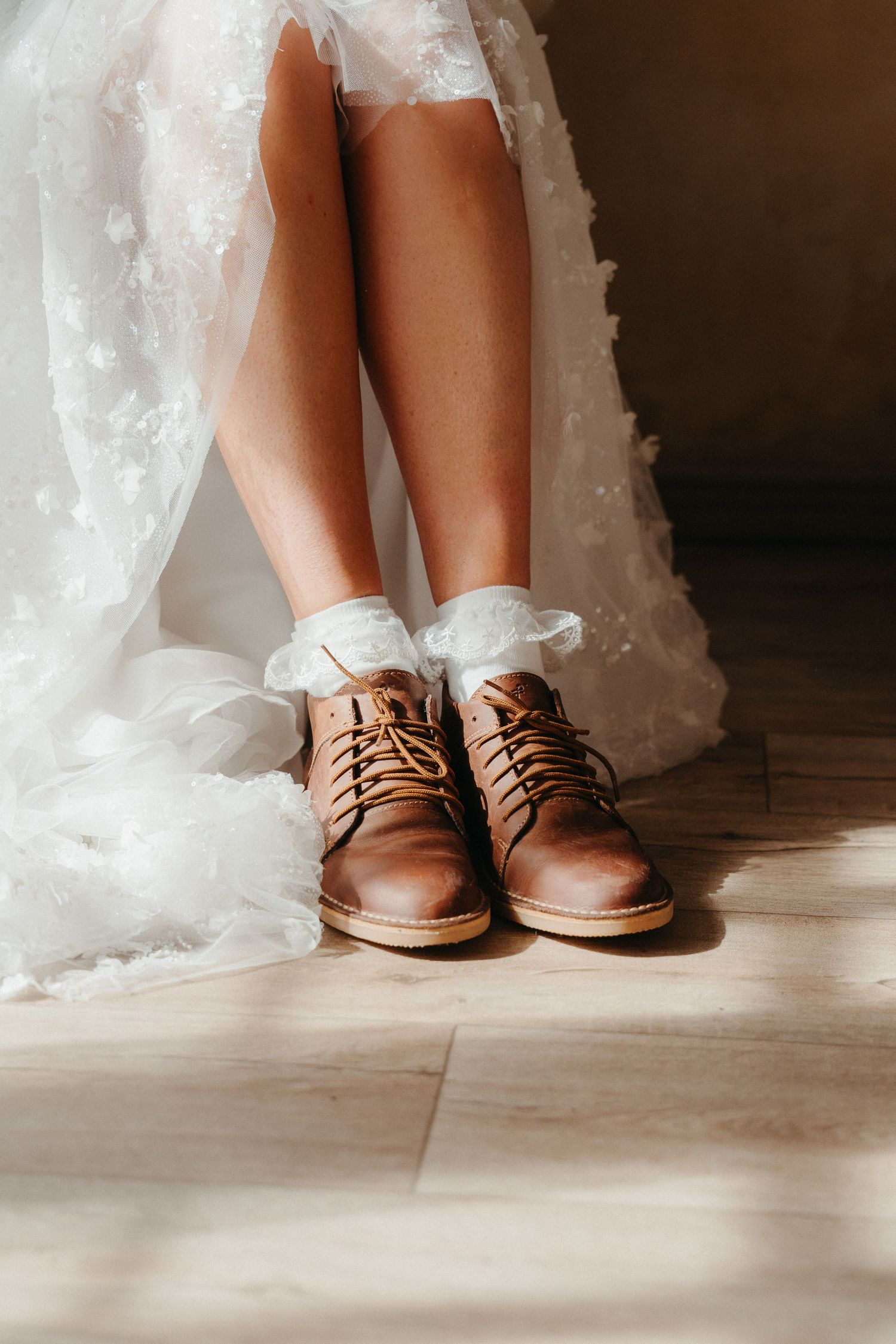 Bride wearing brown leather lace-up boots with white ruffled socks under a flowing white wedding dress.