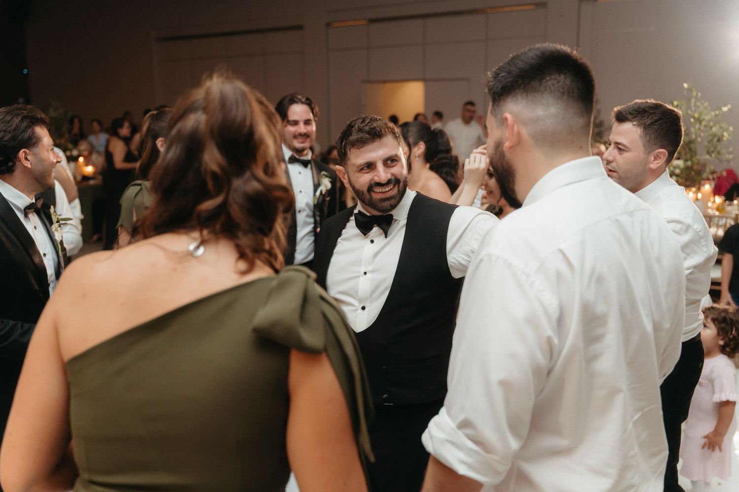 Guests laughing and socializing on the dance floor at an elegant wedding reception in formal attire.