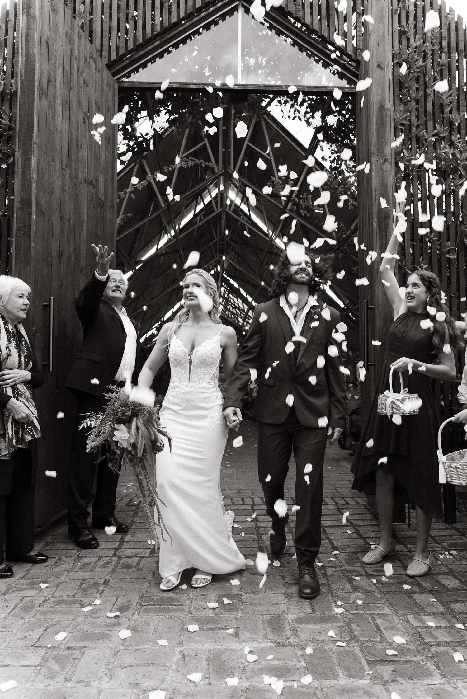 Black and white photo of a bride and groom exiting a church as guests toss flower petals in celebration.