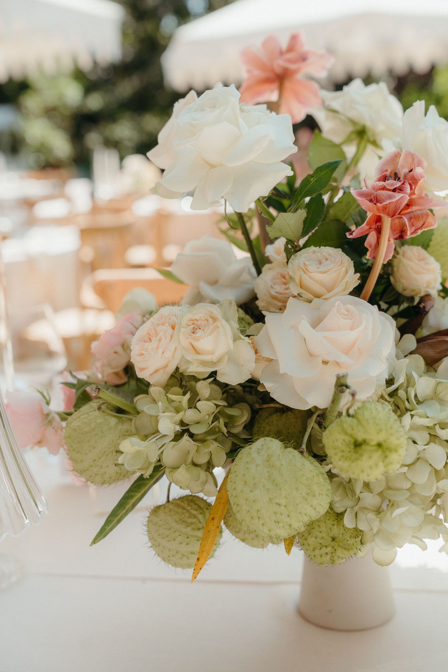 Elegant wedding centerpiece featuring white roses, blush blooms, hydrangeas, and greenery in a white vase on a reception table.