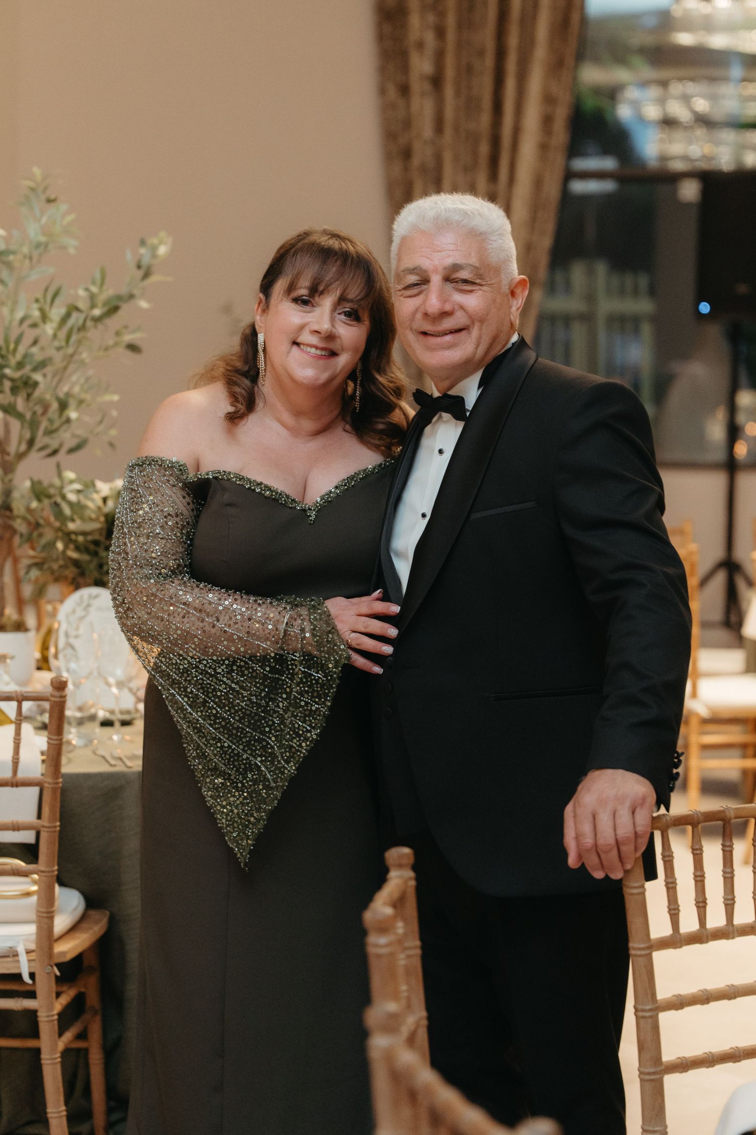 Elegant couple posing at formal event, woman in sparkly off-shoulder gown, man in classic black tuxedo.