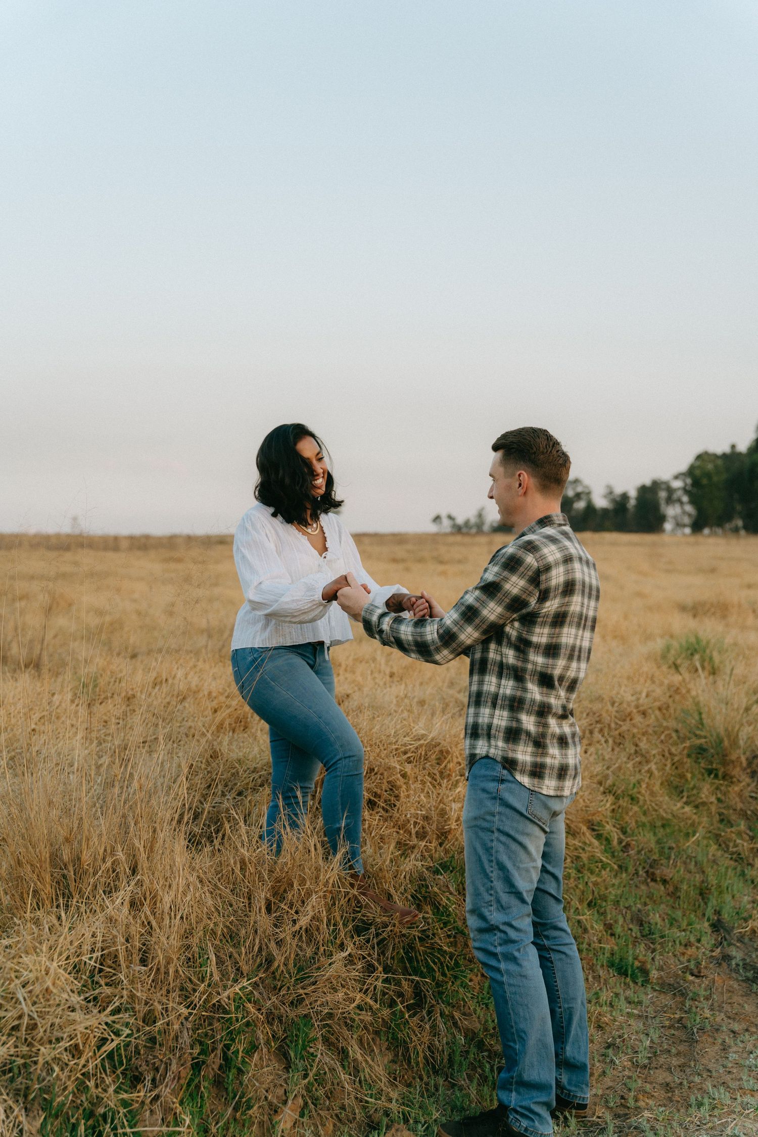 Couple holding hands and laughing together in a golden field in Johannesburg during an outdoor photo session.