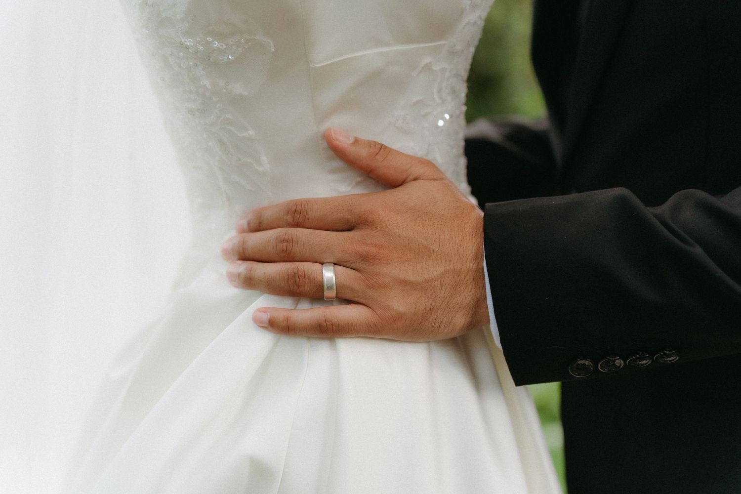 Close-up detail shot of a hand wearing a wedding ring against a white wedding dress.
