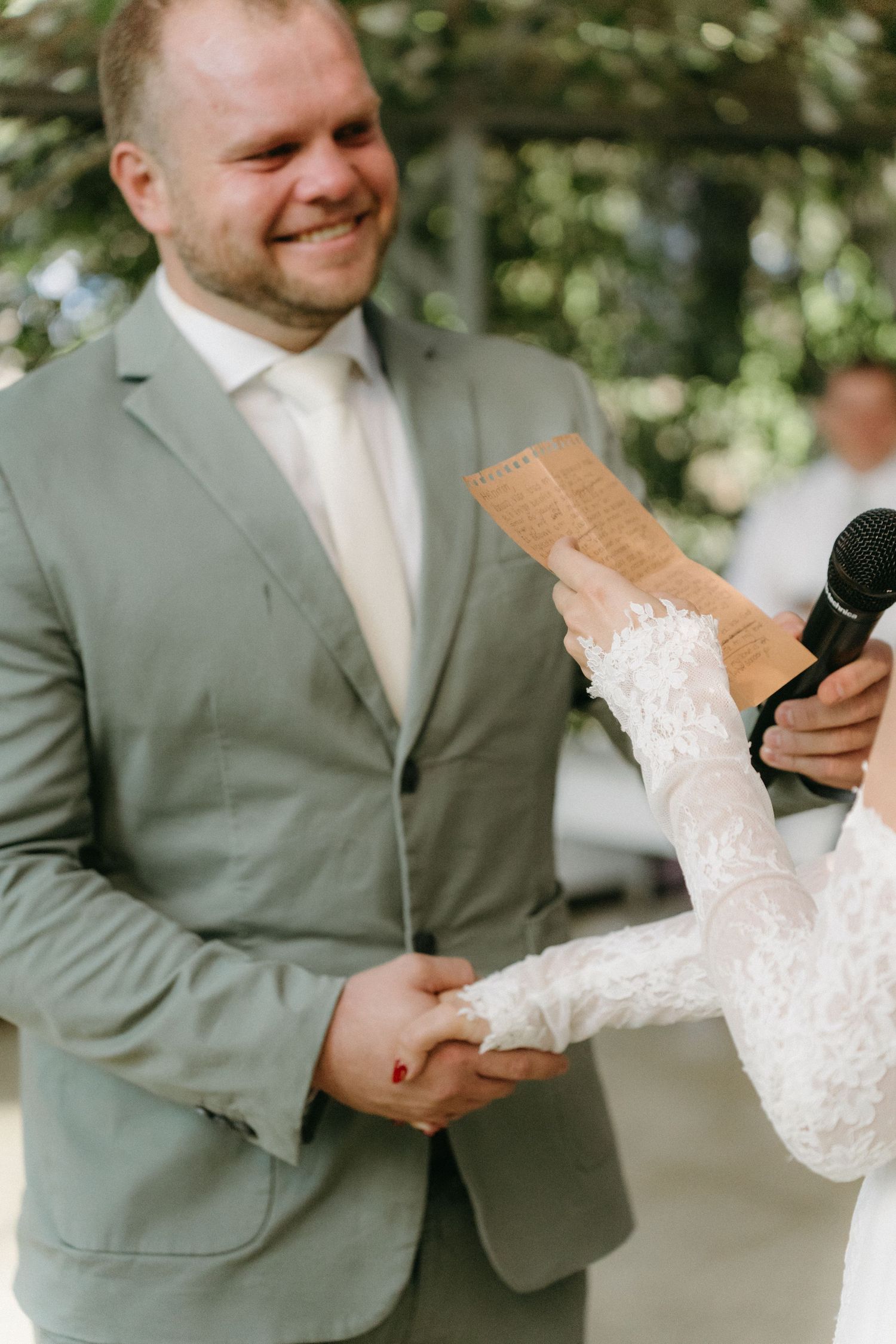 Couple holding hands during wedding vow exchange with groom in light gray suit.