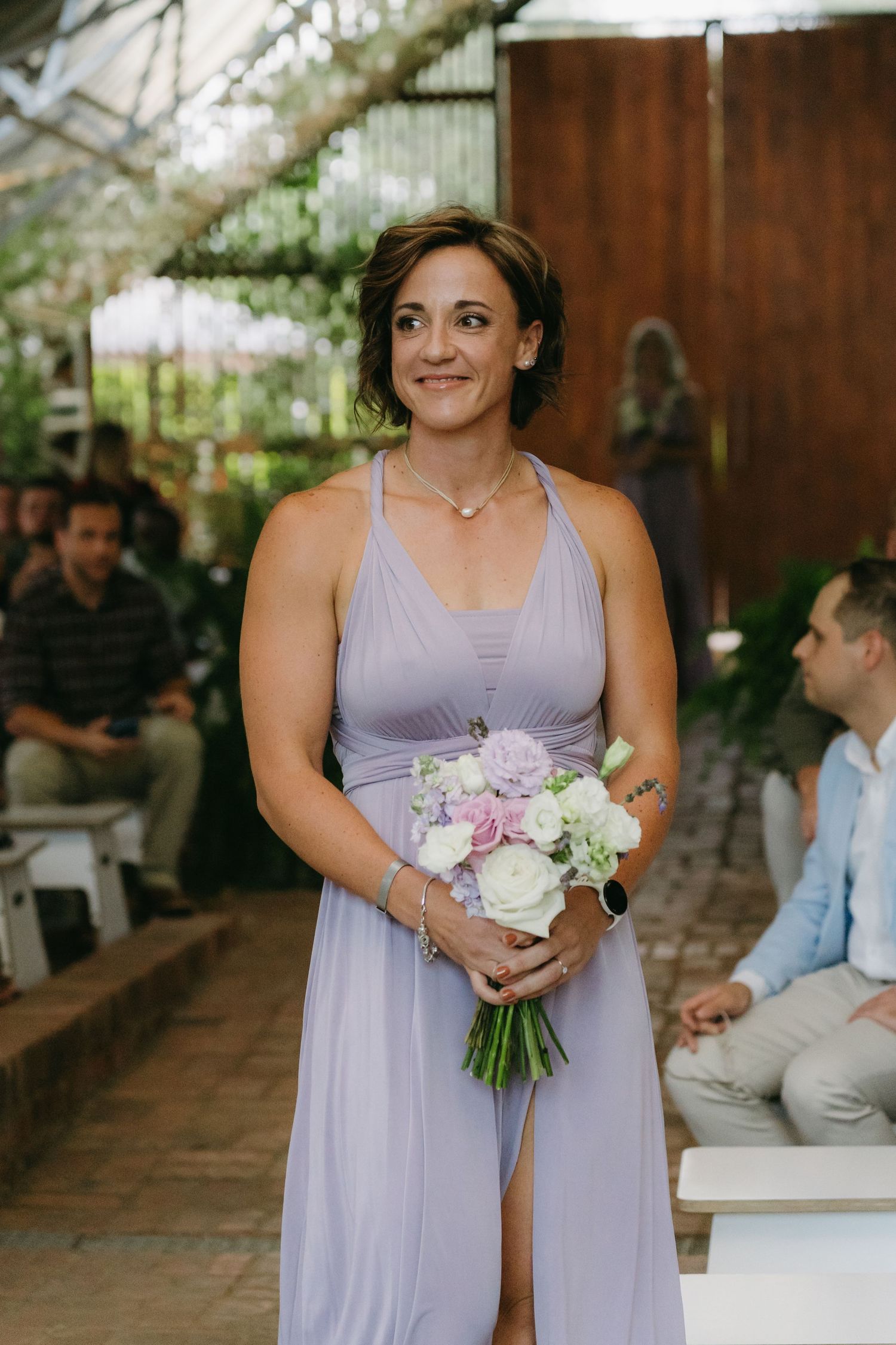 Bridesmaid in a flowing lavender dress holds a delicate bouquet of pink and white flowers at an outdoor garden wedding.