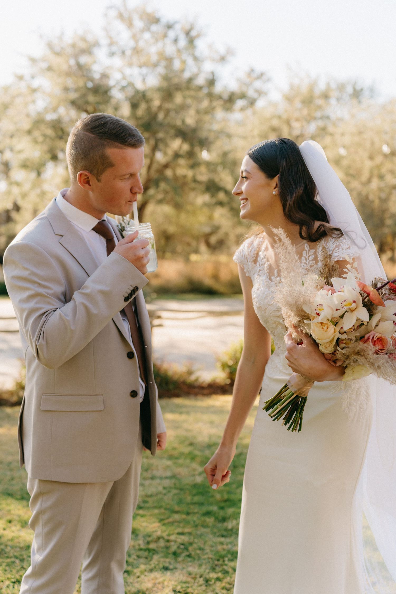 A joyful wedding couple shares a tender moment in an outdoor setting with warm sunlight and natural surroundings.