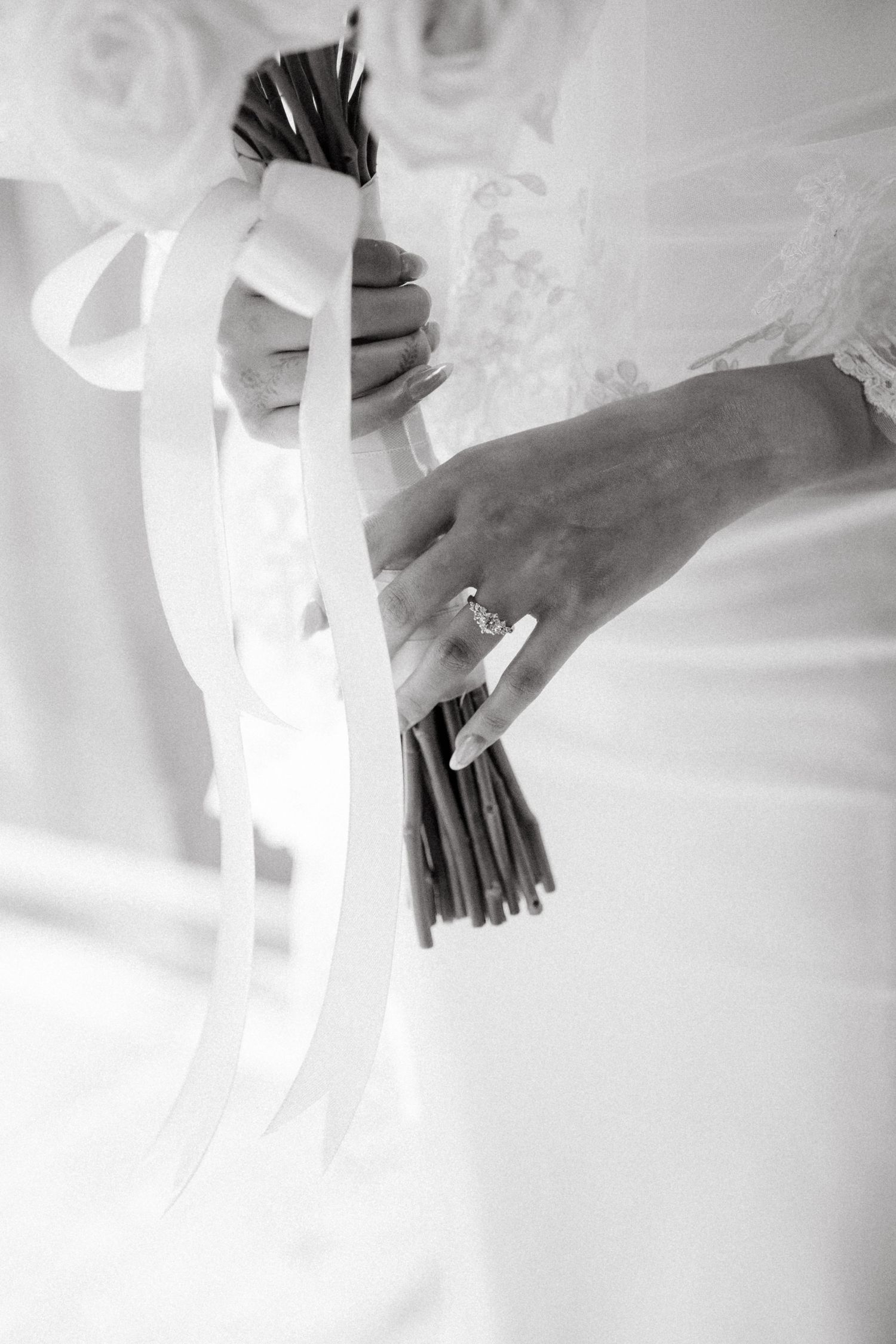 Black and white detail shot of hands holding a wedding bouquet with ribbons.