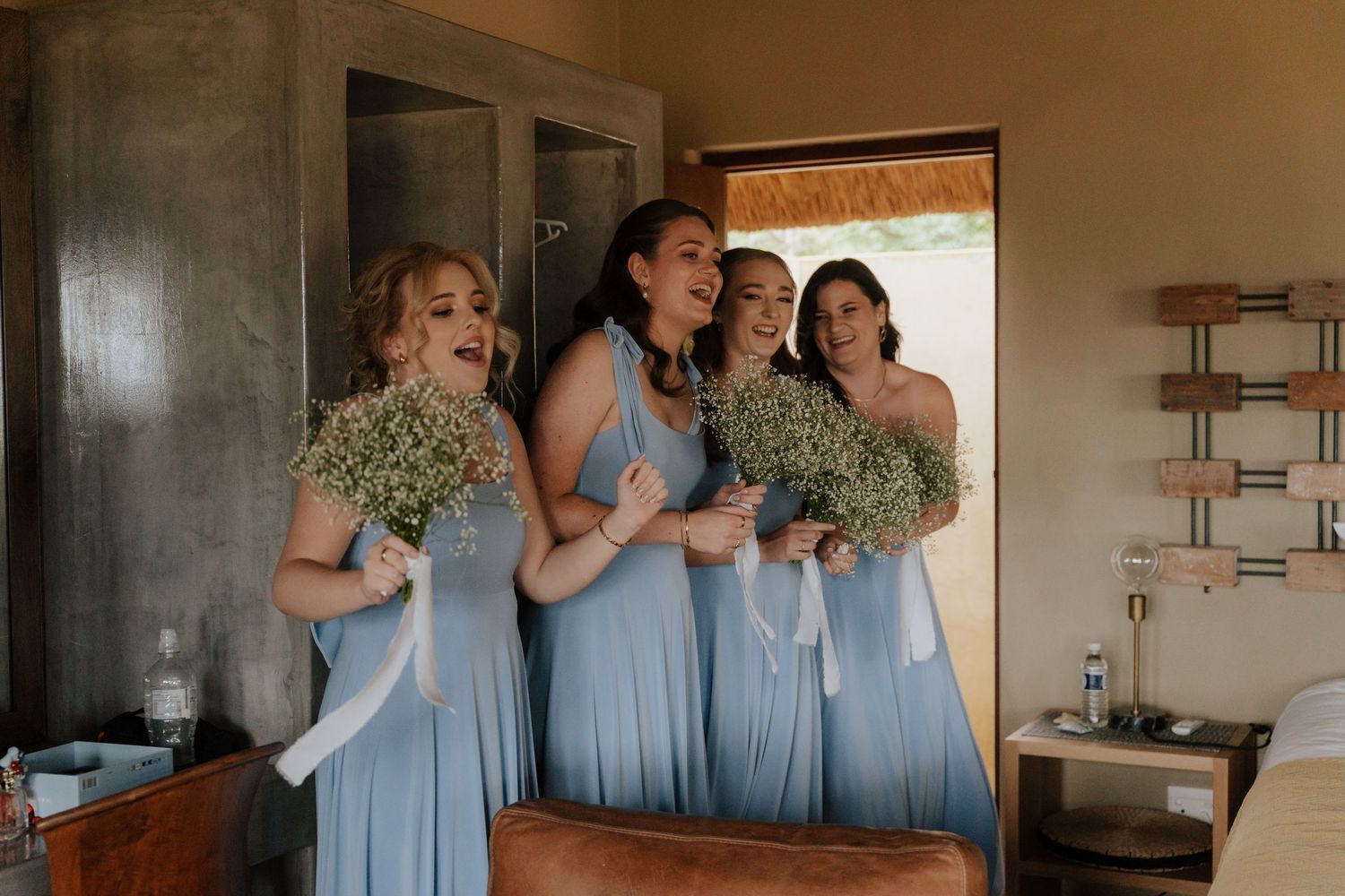 Bridesmaids in flowing light blue dresses gather near a window in preparation for the ceremony.