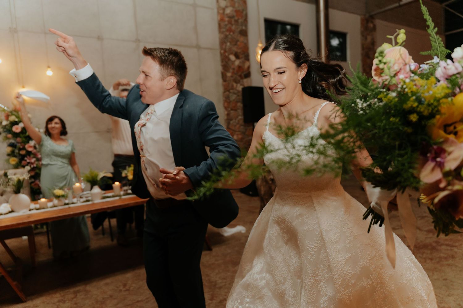 Newlyweds share their first dance at a rustic indoor wedding reception with string lights and floral decorations.