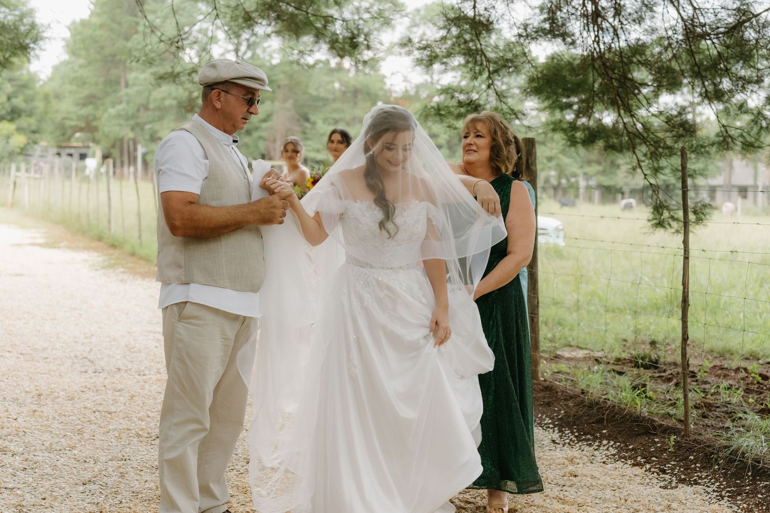 Wedding party walks together on a gravel path outdoors with green foliage in the background.