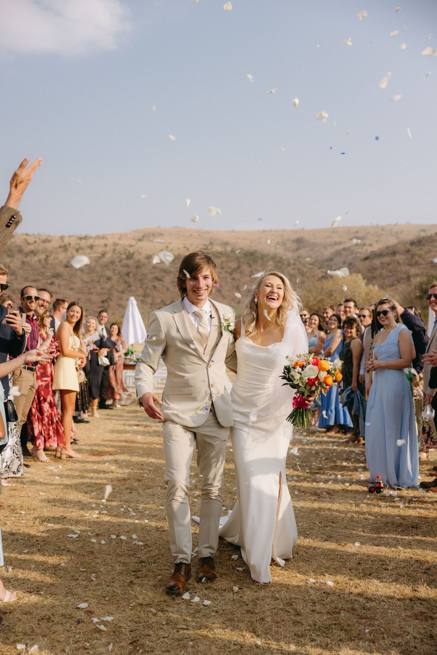Newlyweds celebrate with confetti during their outdoor wedding recessional surrounded by guests.