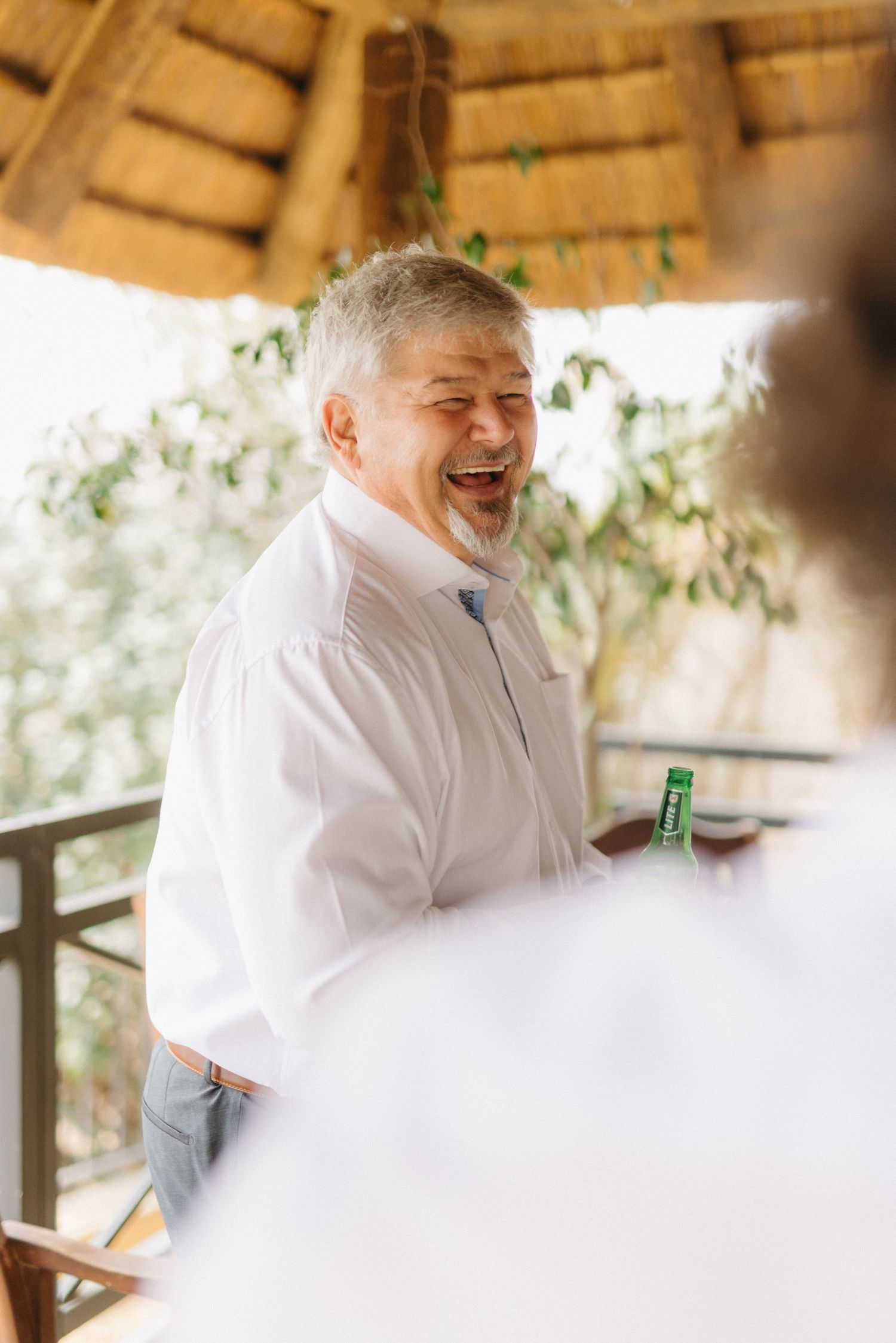 Person in white shirt laughing joyfully under a thatched roof.