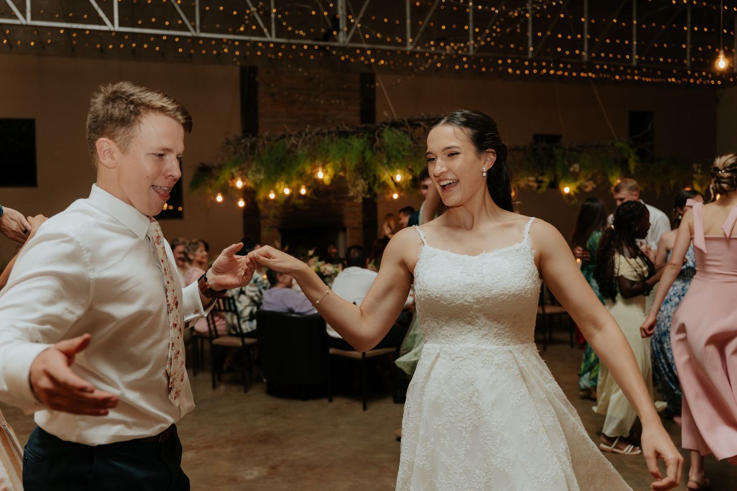 Newlyweds dancing together in an industrial-style reception space with warm lighting and string lights.