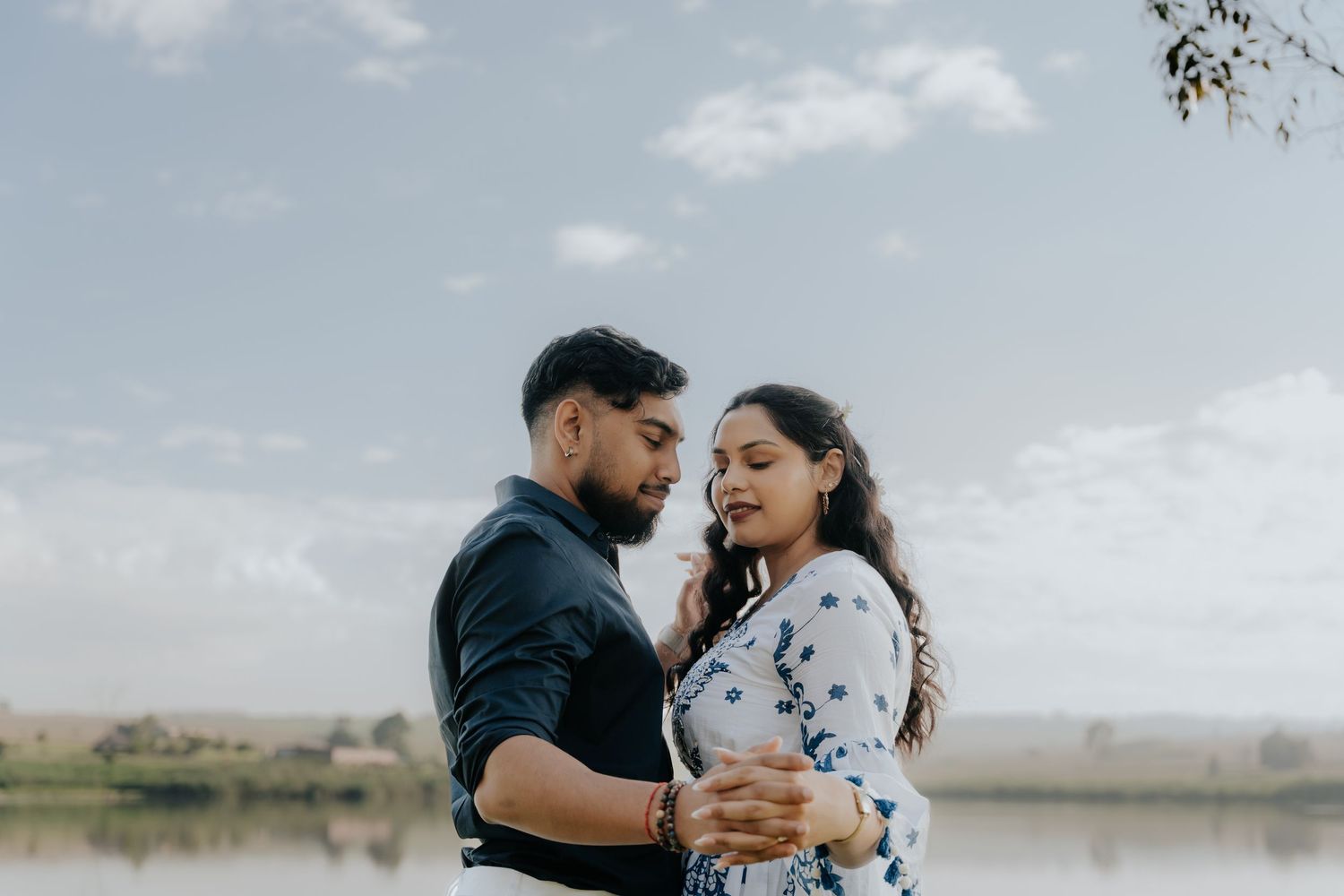 Couple embraces in romantic outdoor photoshoot series with cloudy sky backdrop.