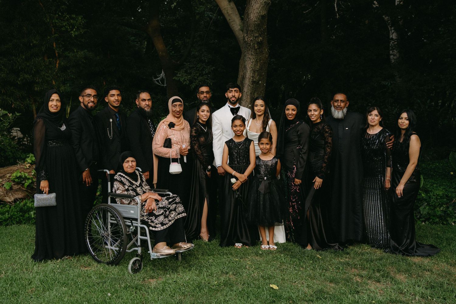 Wedding guests gather for a group photo outdoors wearing coordinated formal black attire.