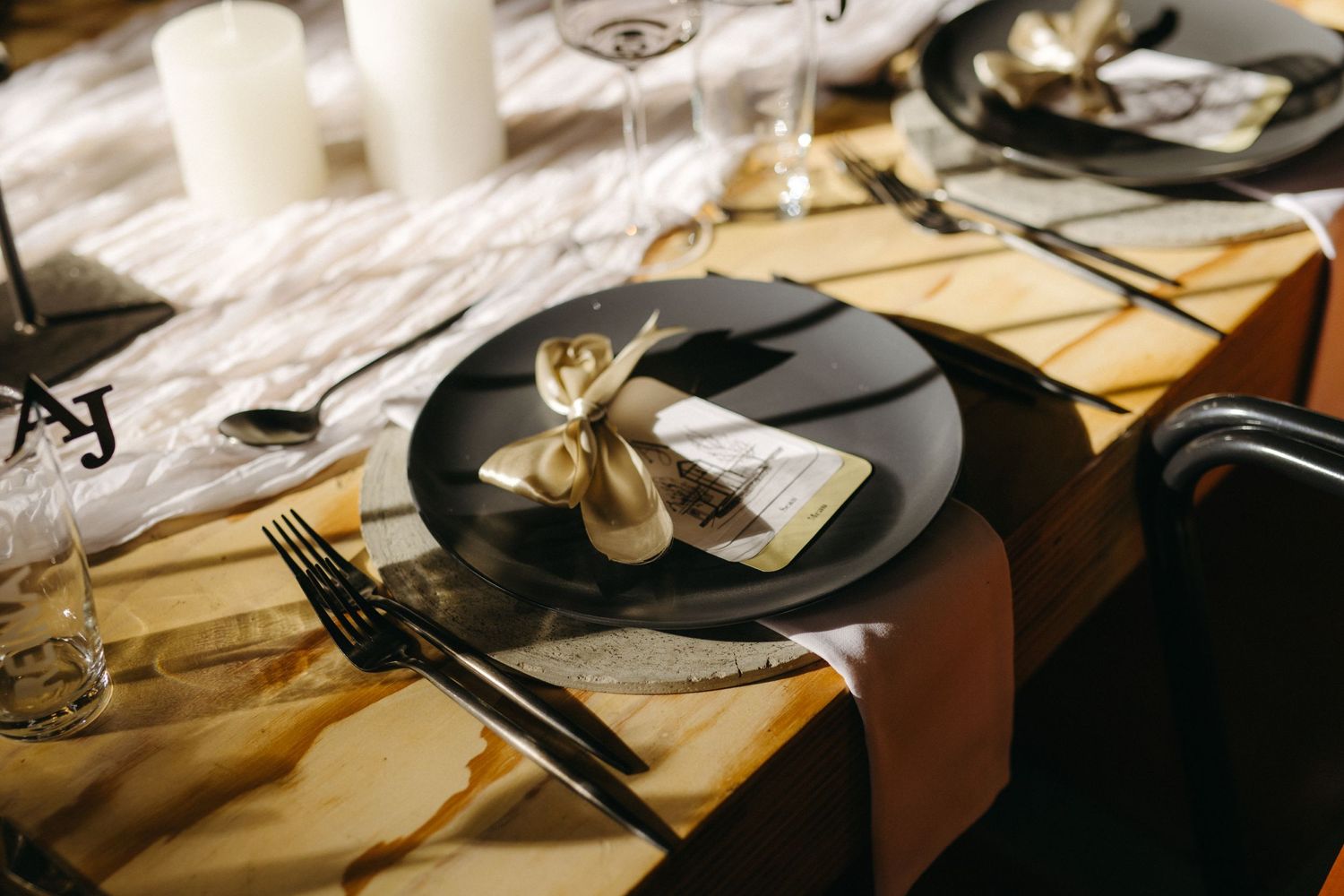 Modern table setting with dark plates, gold accents, and white linens for an elegant dinner party.