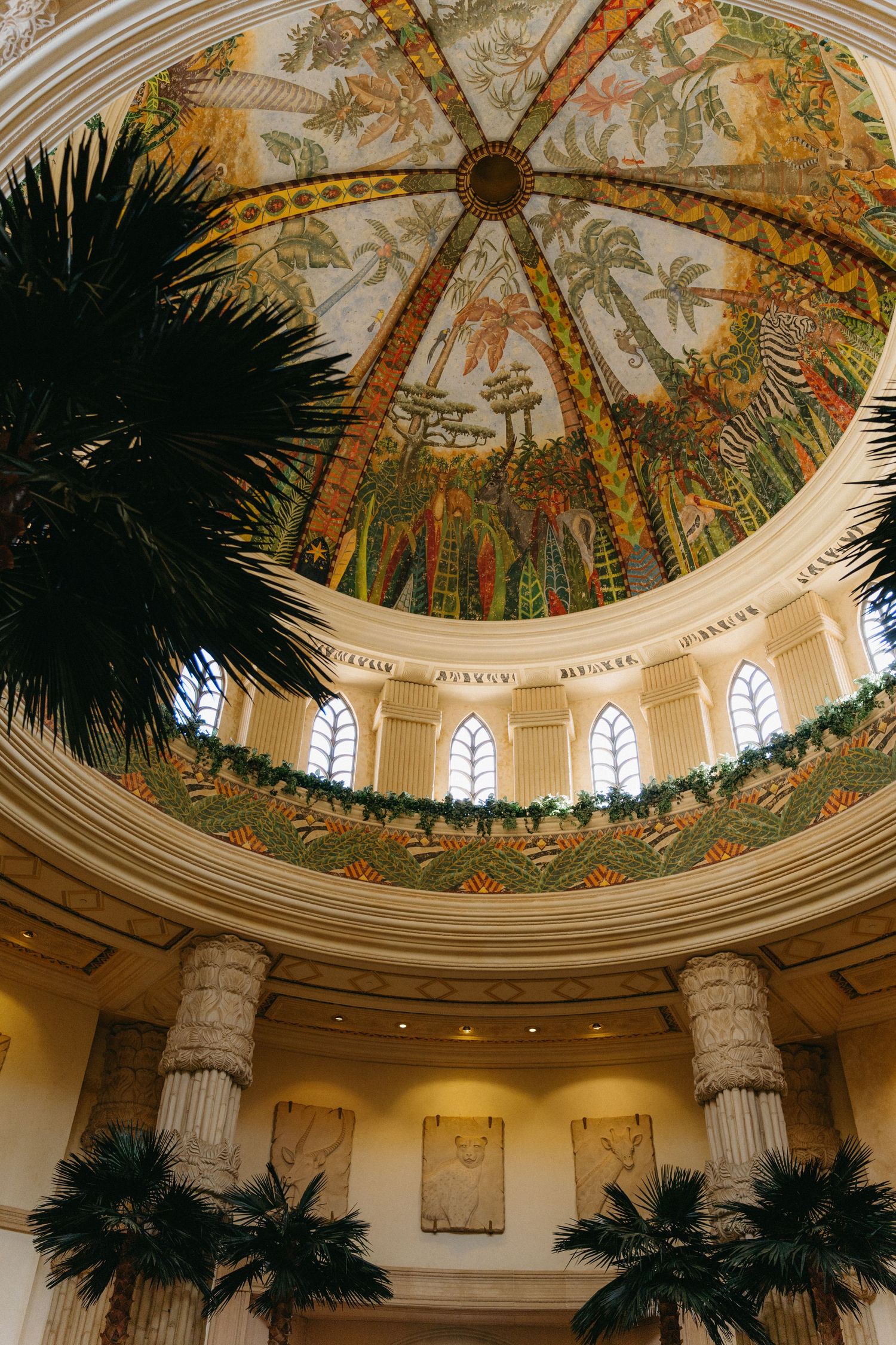 Ornate domed ceiling with palm trees and intricate painted tropical murals in a grand circular rotunda.