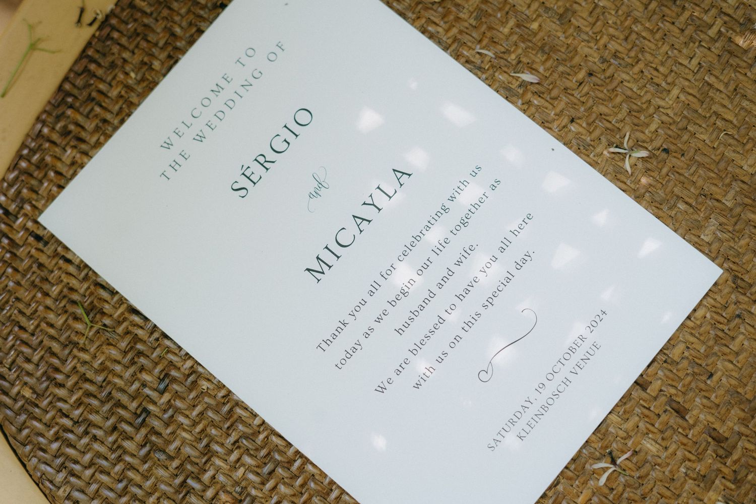 Wedding invitation details printed in elegant typography on white paper photographed against a burlap textured background.