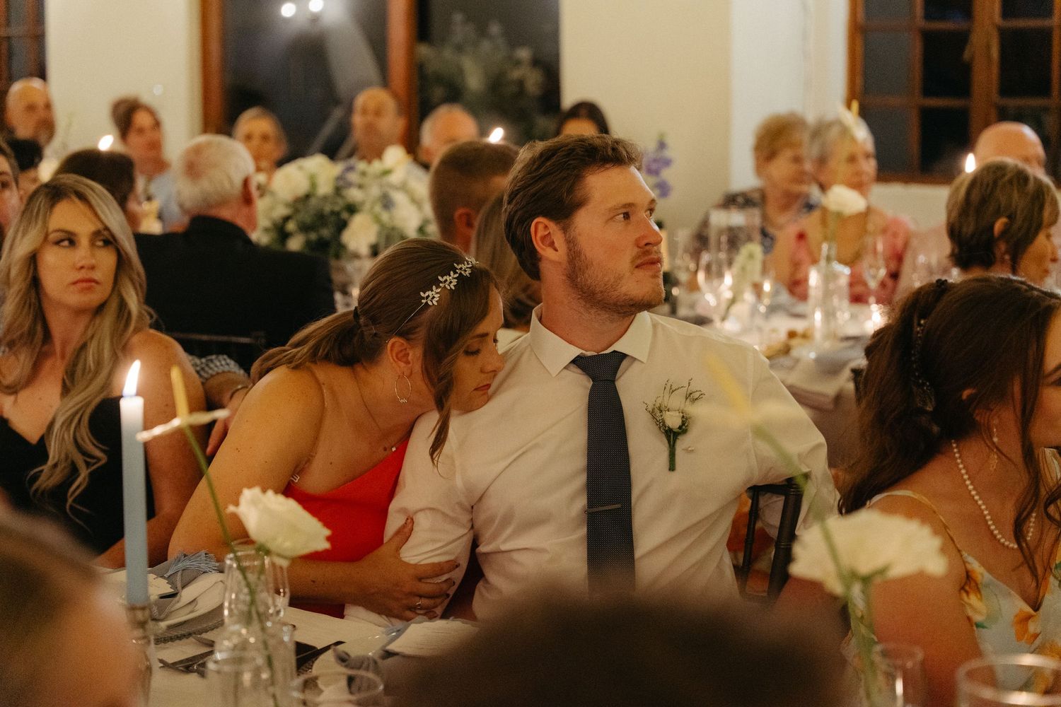 Wedding reception guests seated at long tables in a warmly lit banquet hall during evening celebrations.