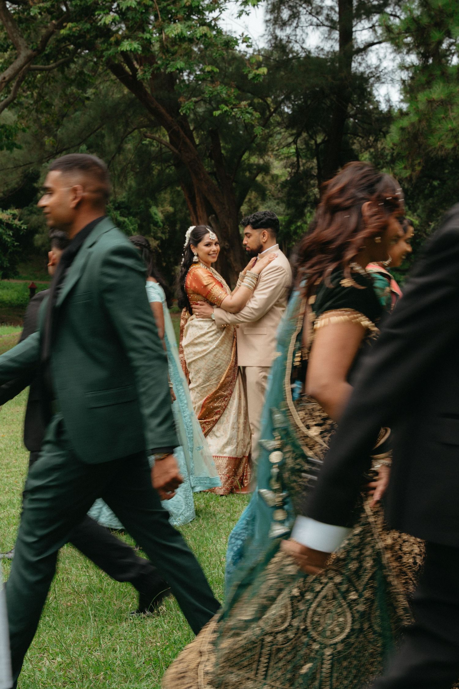 Wedding party walks and dances together on grassy lawn during outdoor celebration.