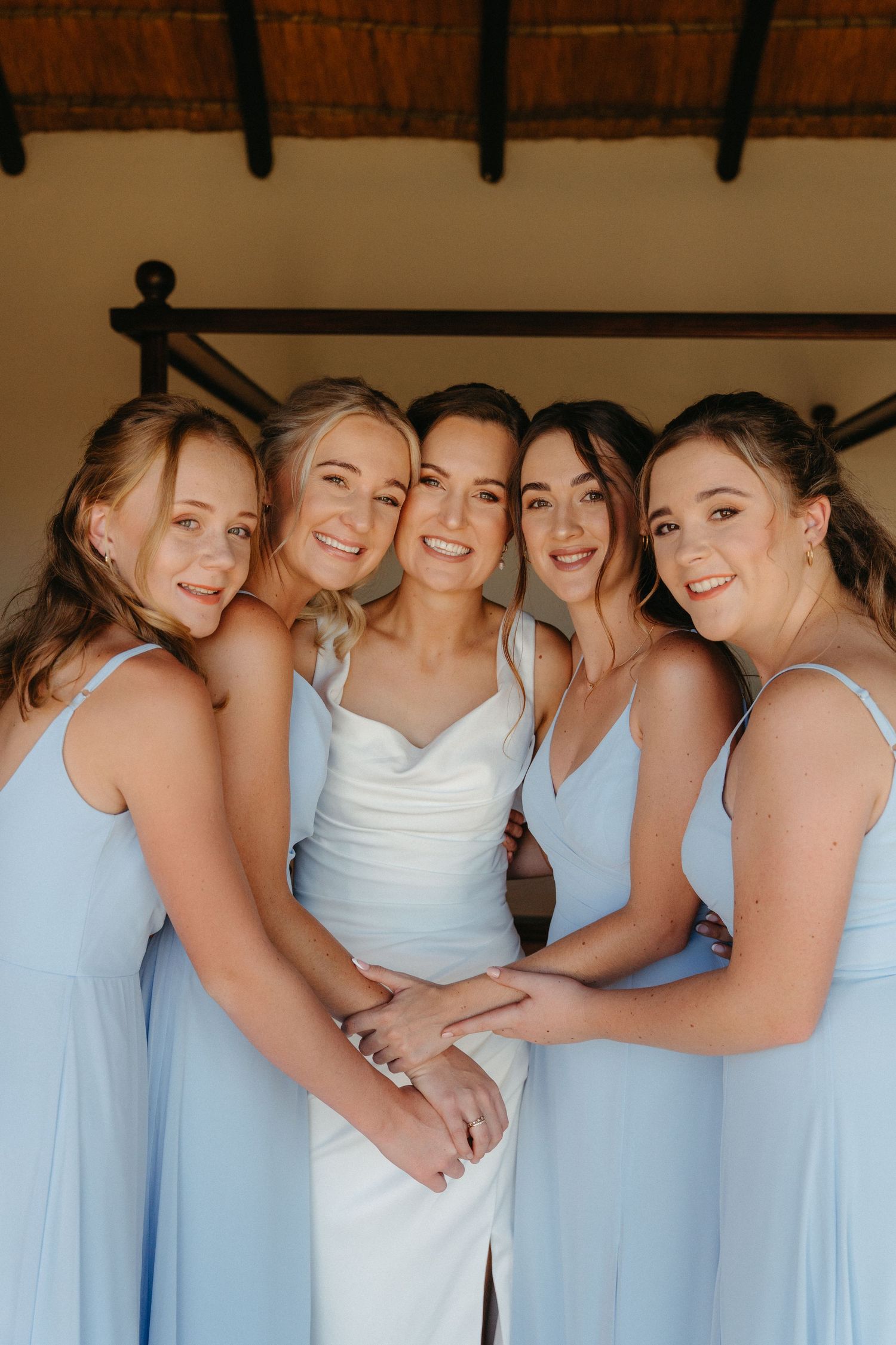 A group of bridesmaids in light blue dresses and white gowns gather together for a wedding photo.