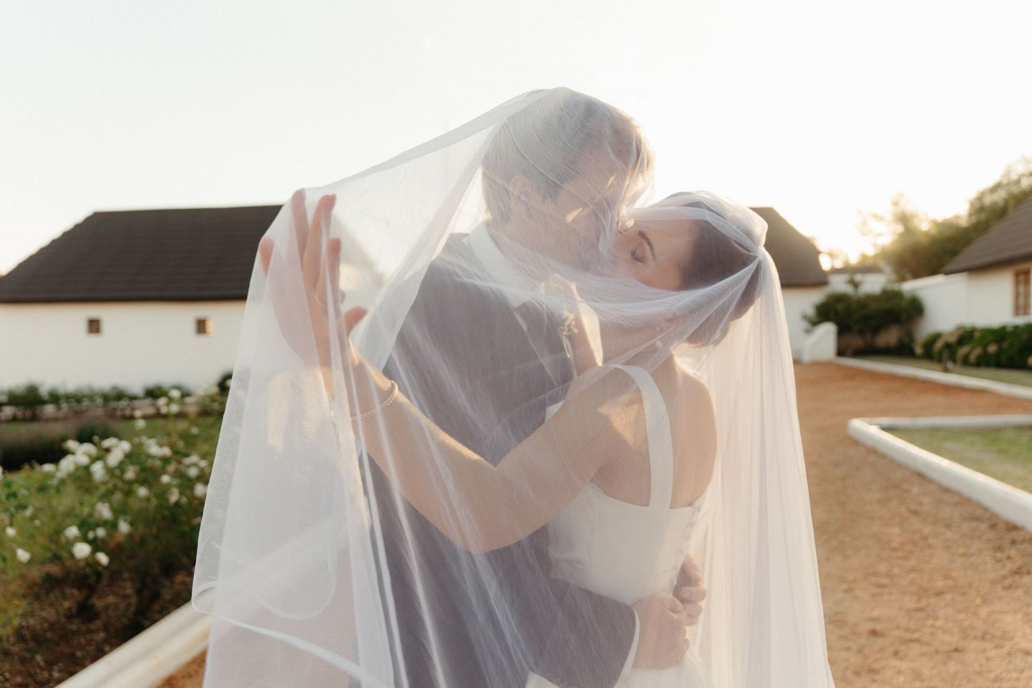 A romantic couple shares a tender moment under a flowing white veil at sunset.