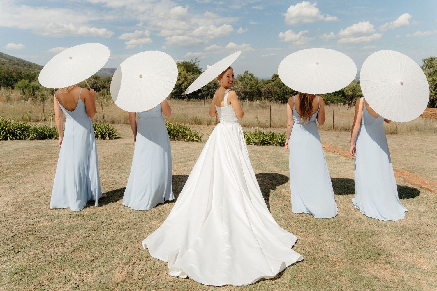 A series of flowing white dresses in an outdoor field setting creates an ethereal sequence of movement and grace.