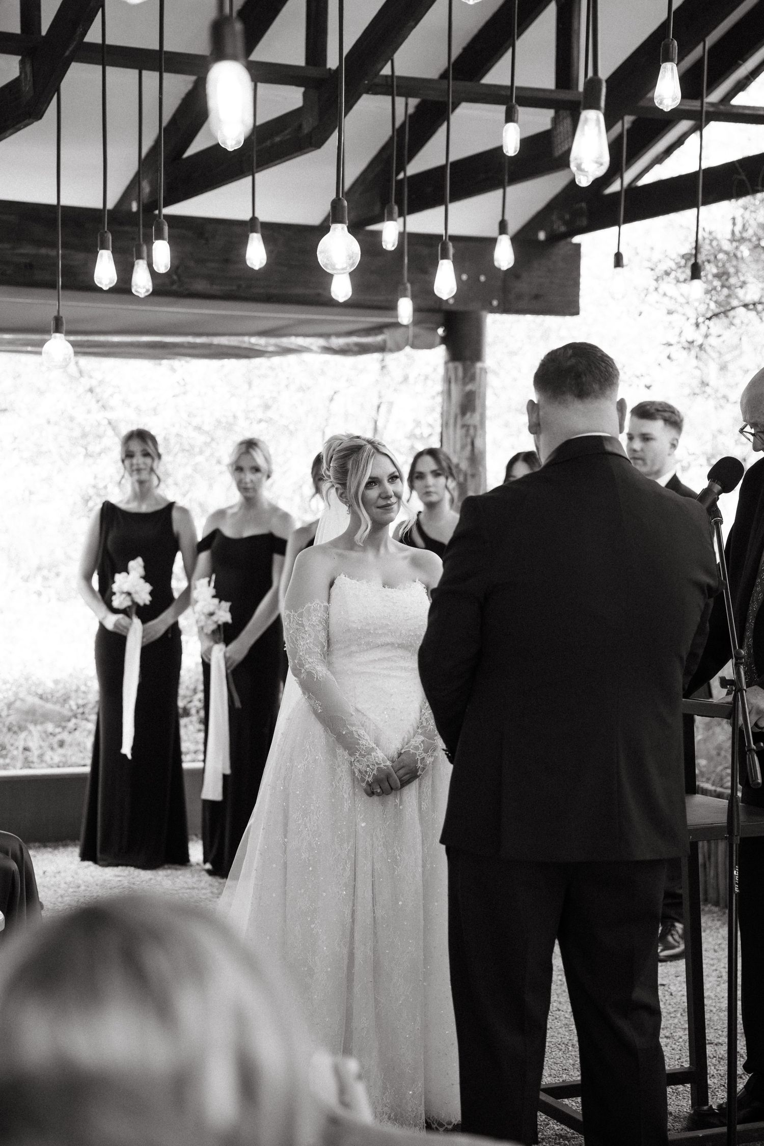 Wedding couples dance together in an elegant indoor venue with hanging lights and exposed beams.