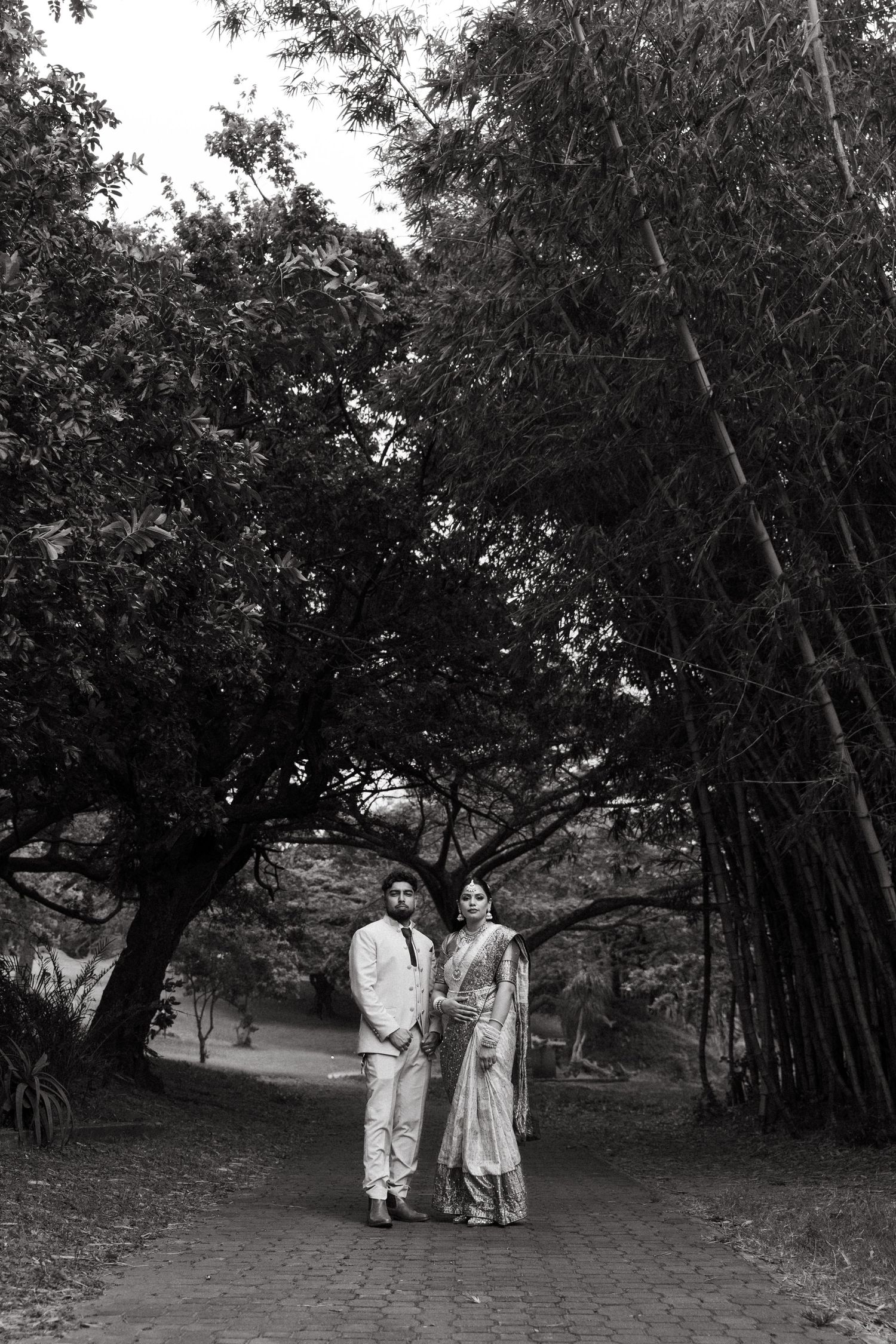 A black and white photo series shows two figures in light-colored clothing walking together near bamboo trees.