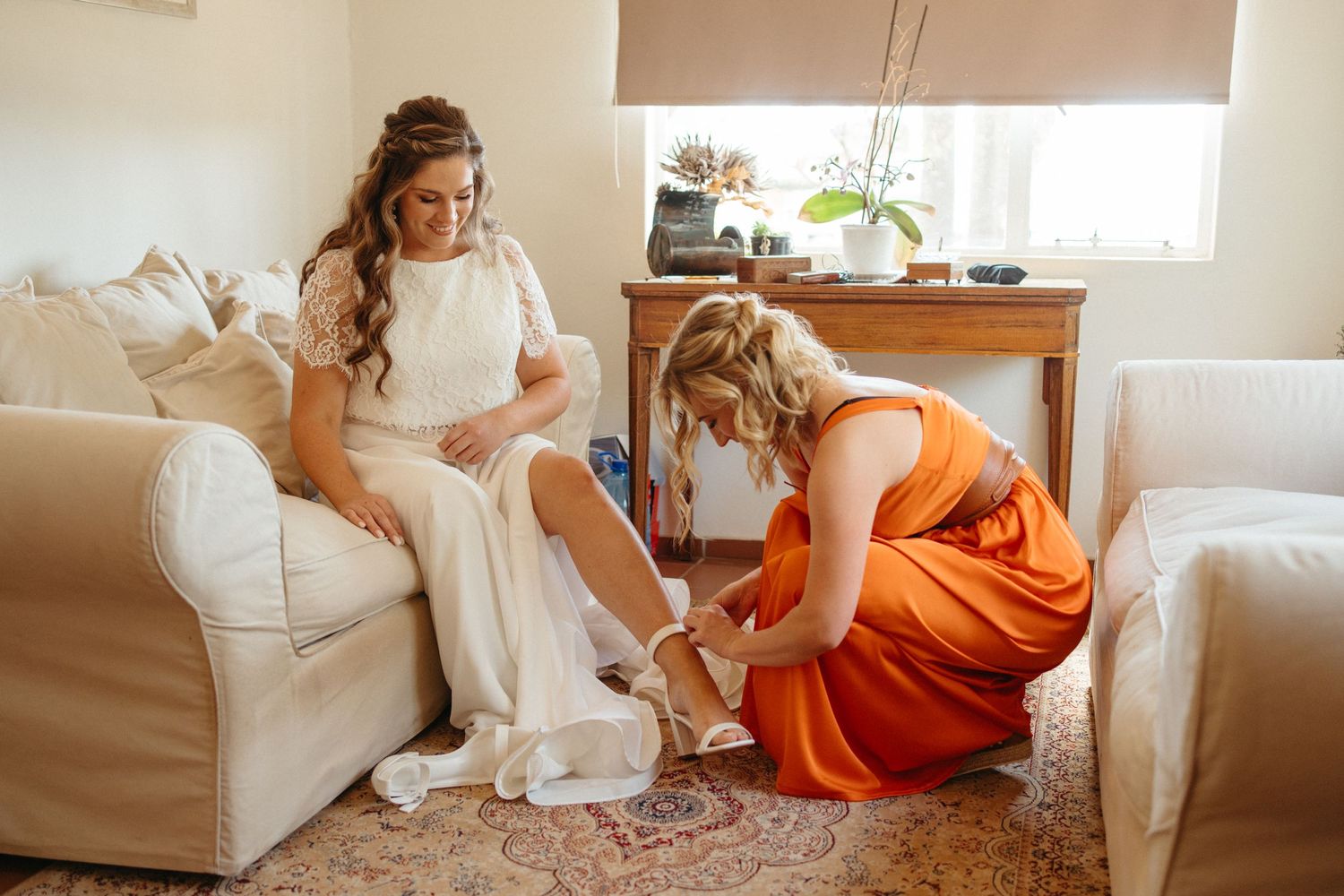 Wedding preparation scene with someone in orange helping adjust the bride's dress.