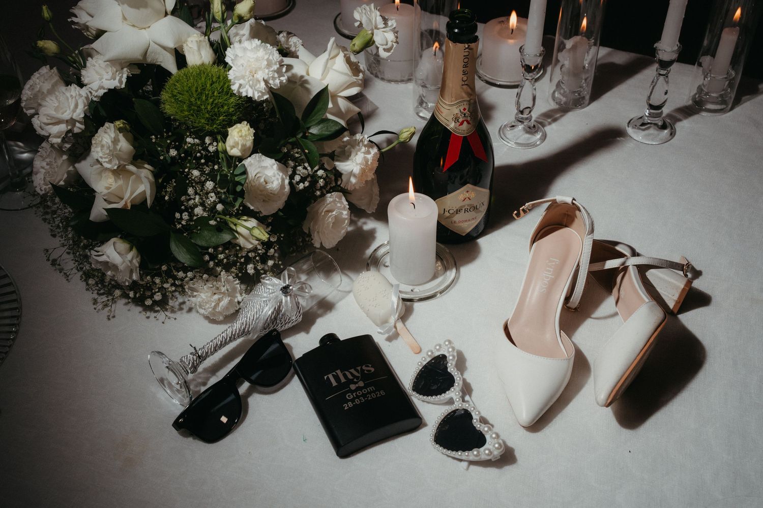 Wedding flat lay with white roses, champagne, heels, and bridal accessories at Bona Bona Lodge