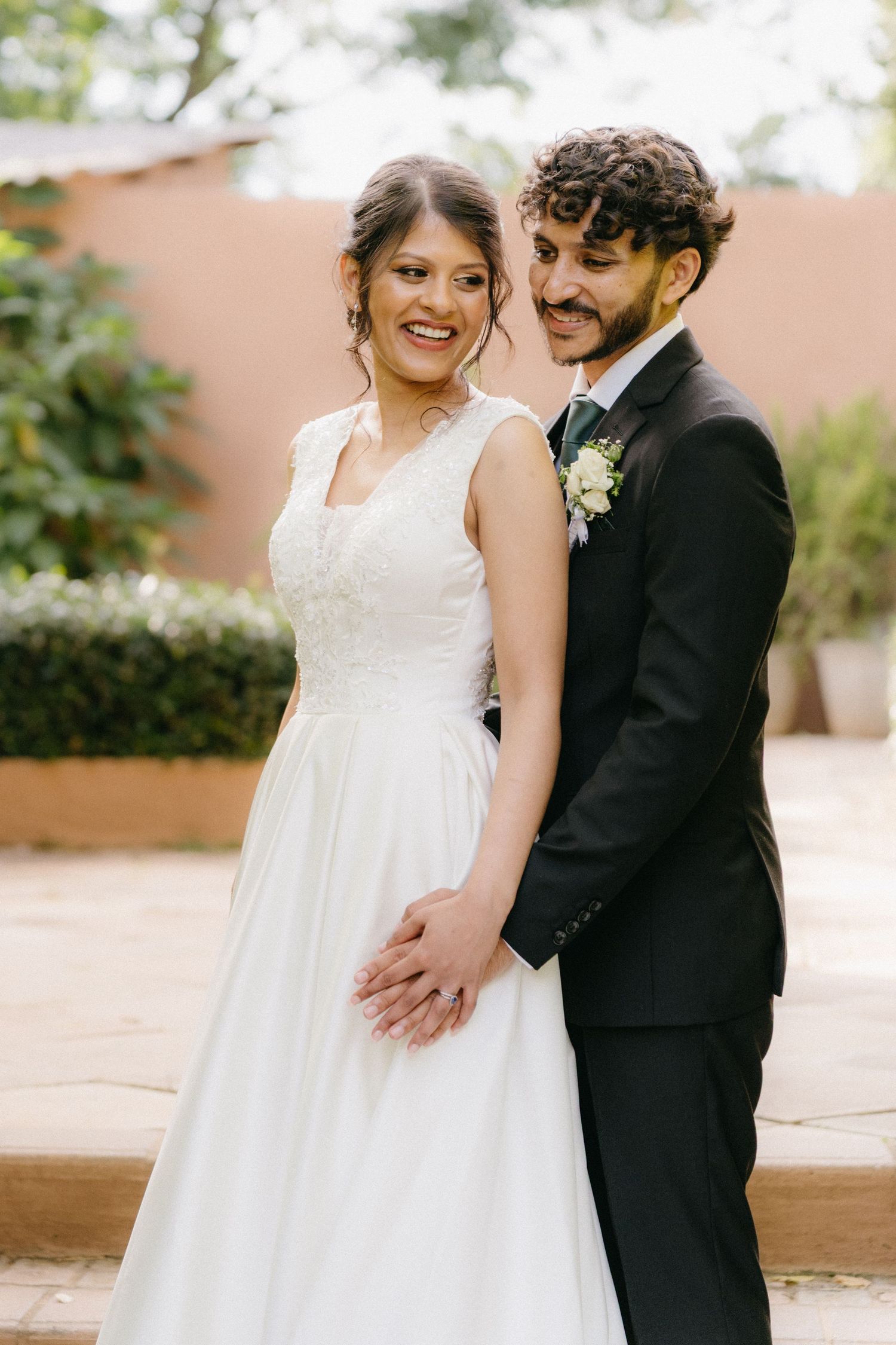 A couple in wedding attire share a joyful moment together in an outdoor garden setting.
